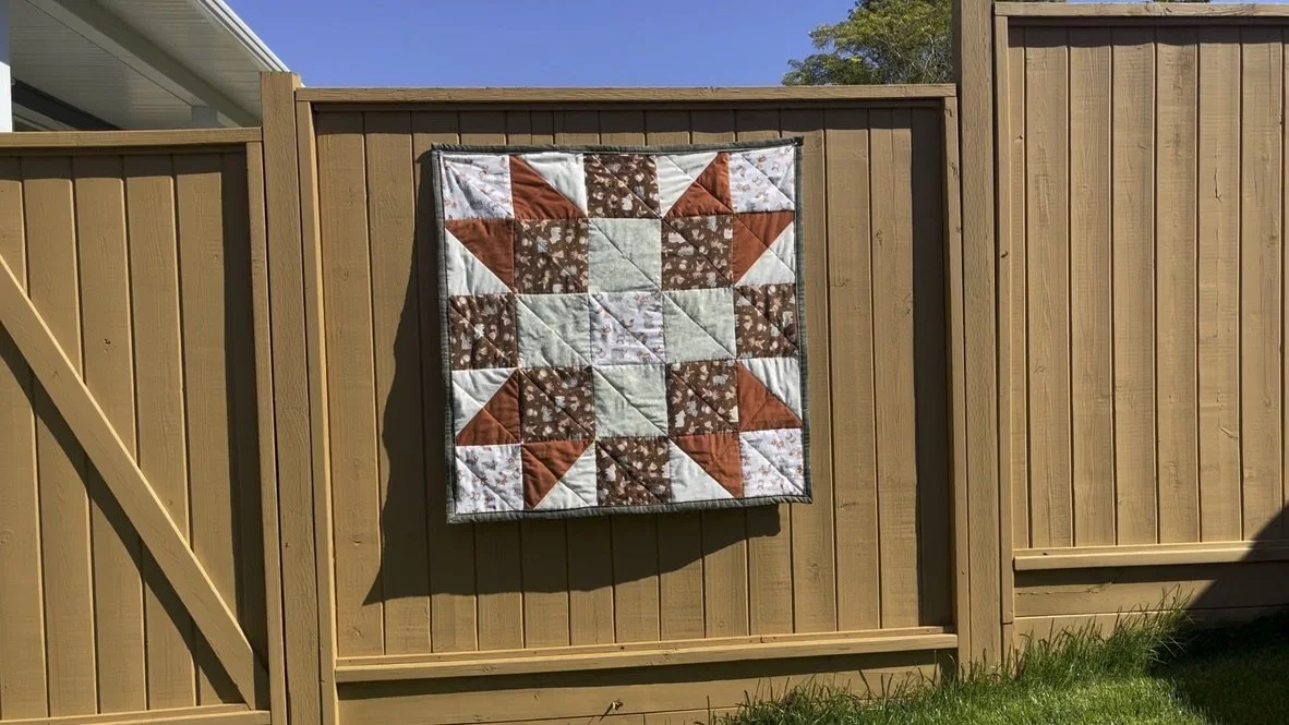 A quilt with a geometric pattern hanging on a wooden fence.