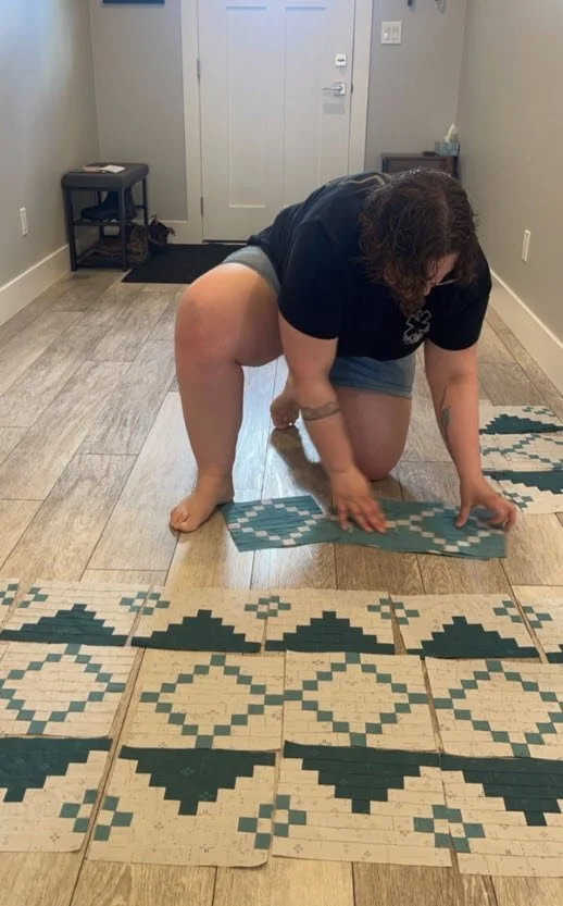 A person with curly hair kneels on the floor arranging patterned tiles in a room with wooden flooring and a white door in the background.