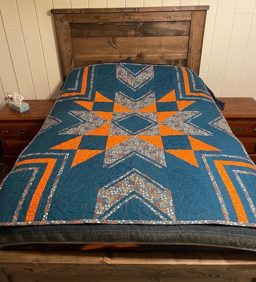 bed with a colorful quilt featuring orange and floral patterns, wooden headboard, and nightstands with tissue box and electrical outlet