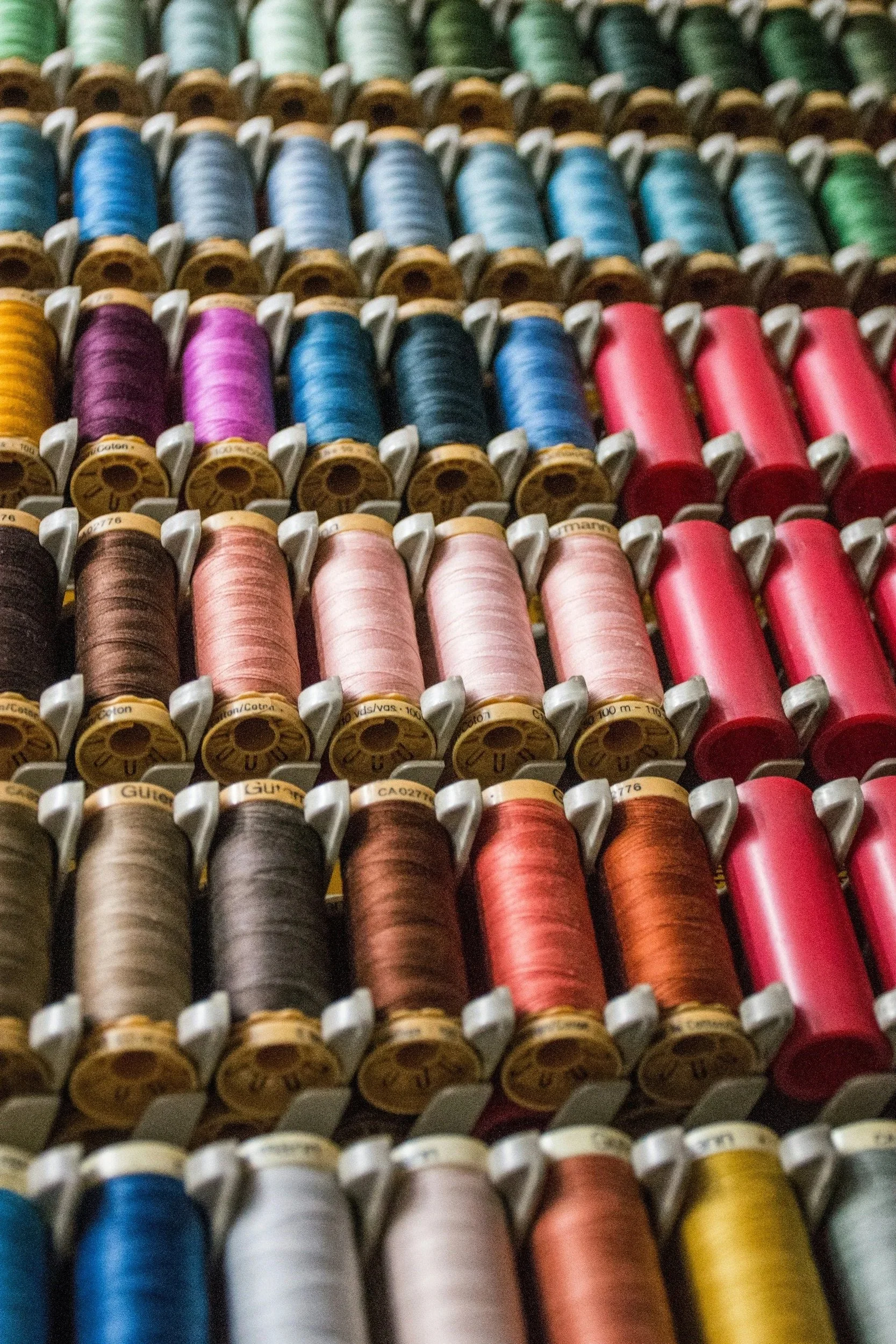 Close-up of various colorful spools of thread arranged in rows.