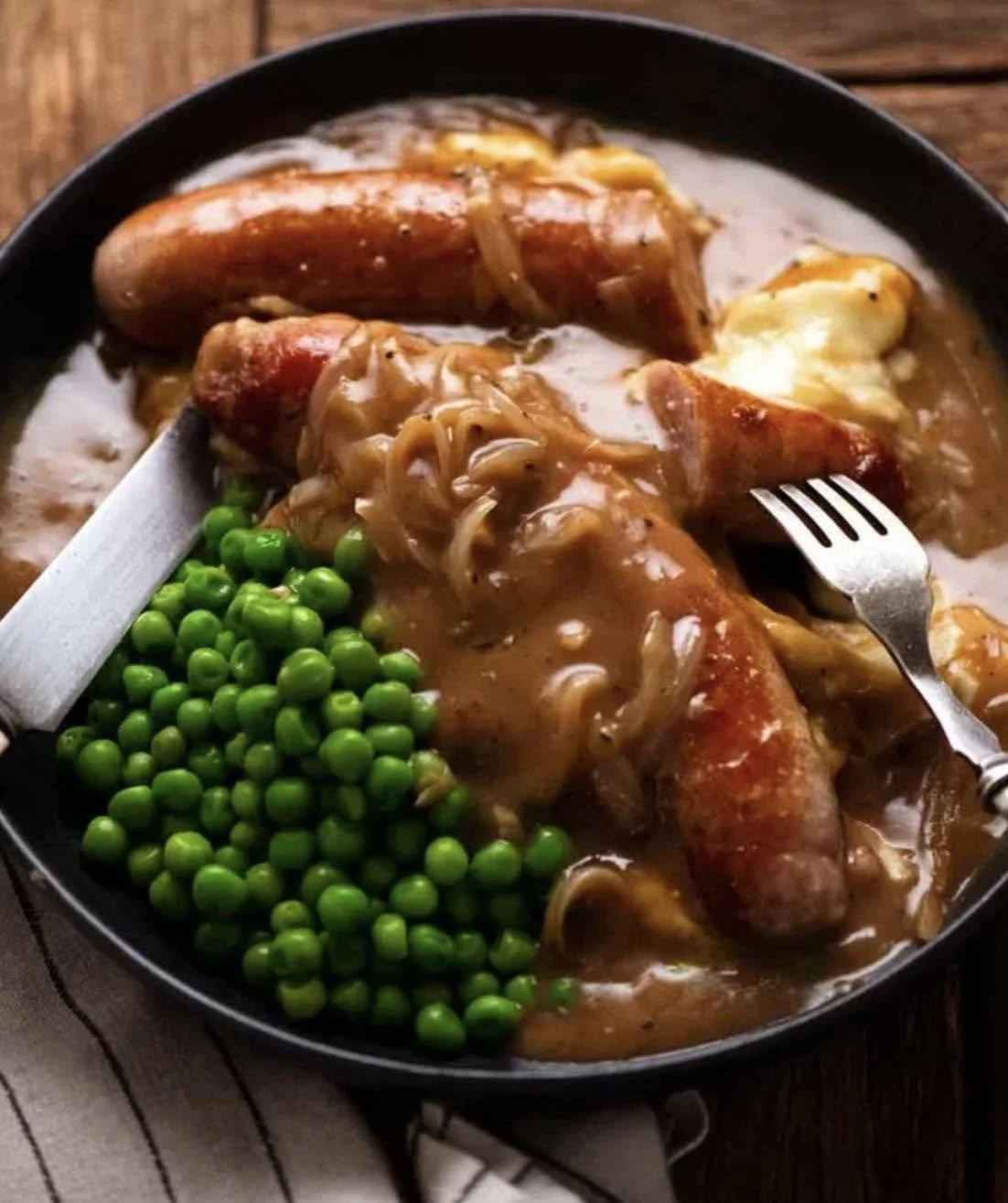 Rabbit legs with gravy, onions, and peas on a black plate.