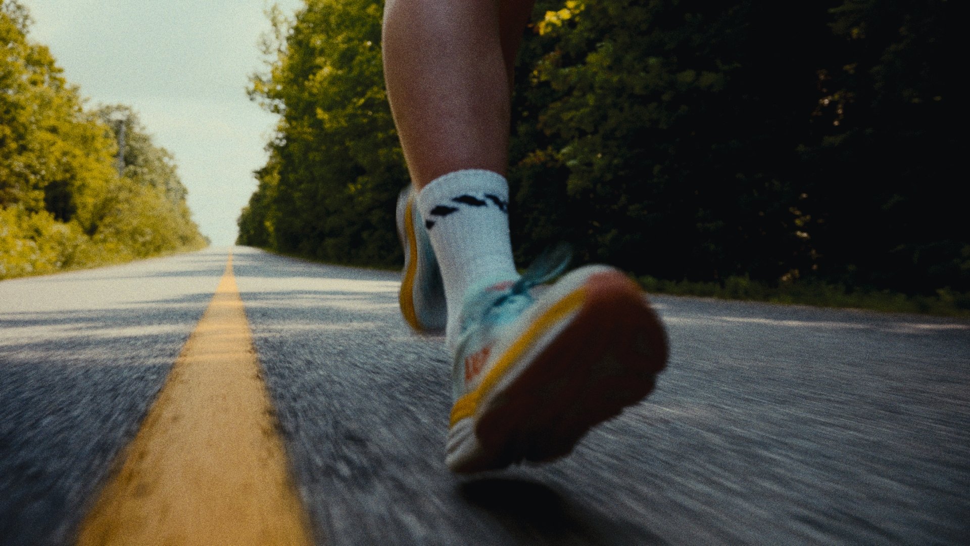 Gros plan d'une chaussure en marche sur une route goudronnée, avec la nature en arrière-plan