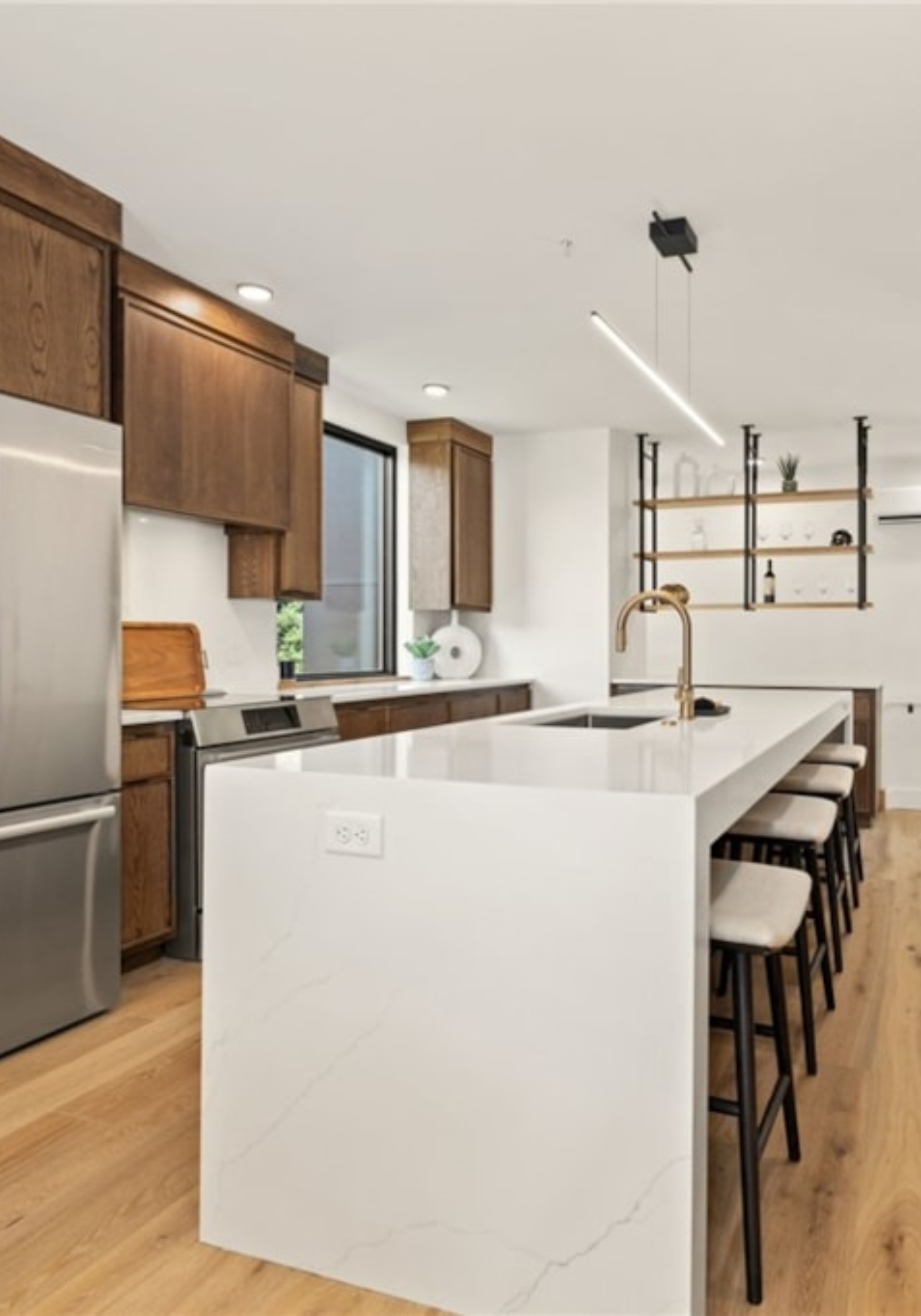 Modern kitchen with white island, wooden cabinets, stainless steel appliances, and open shelving with decorative items.