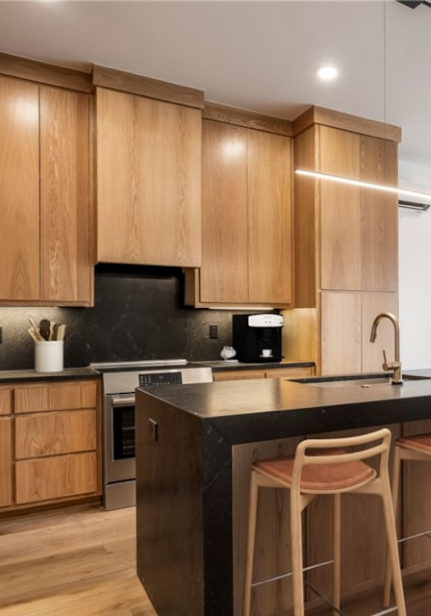 Modern kitchen with wooden cabinets, black countertops, and a kitchen island with two wooden chairs.