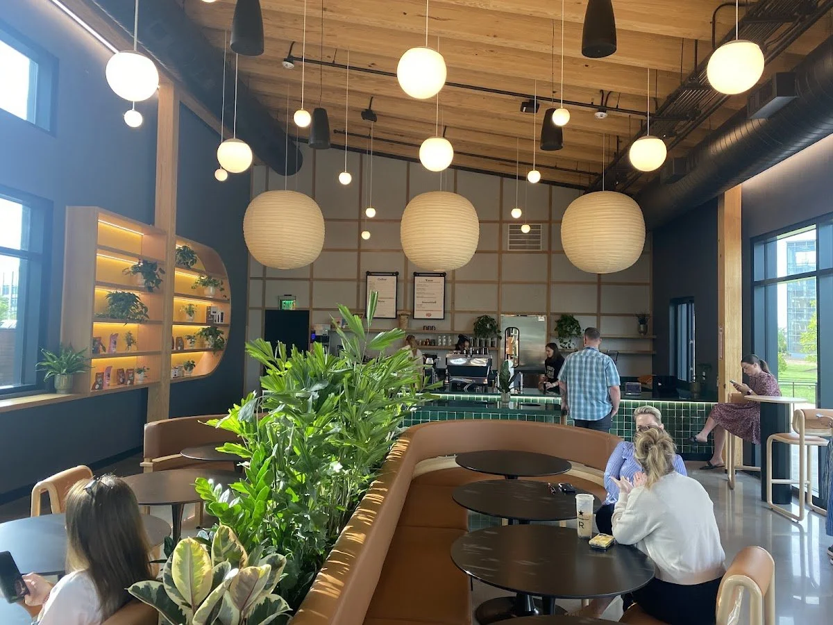Interior of a modern coffee shop with wood accents, hanging lamps, seating area, and customers using laptops and phones.
