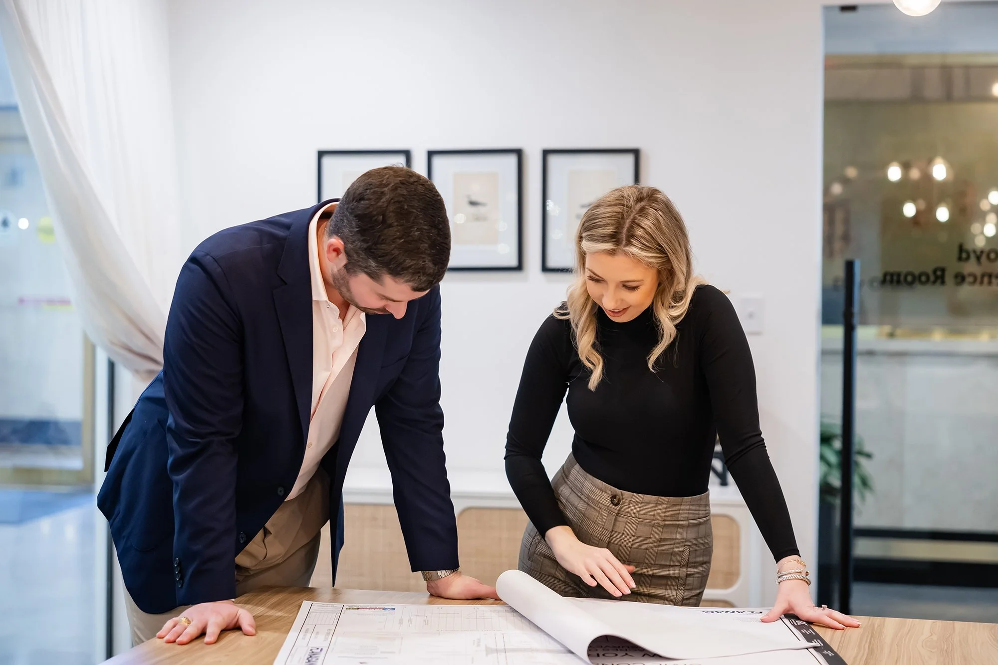 Two professionals, a man and a woman, reviewing documents on a table in a modern office.