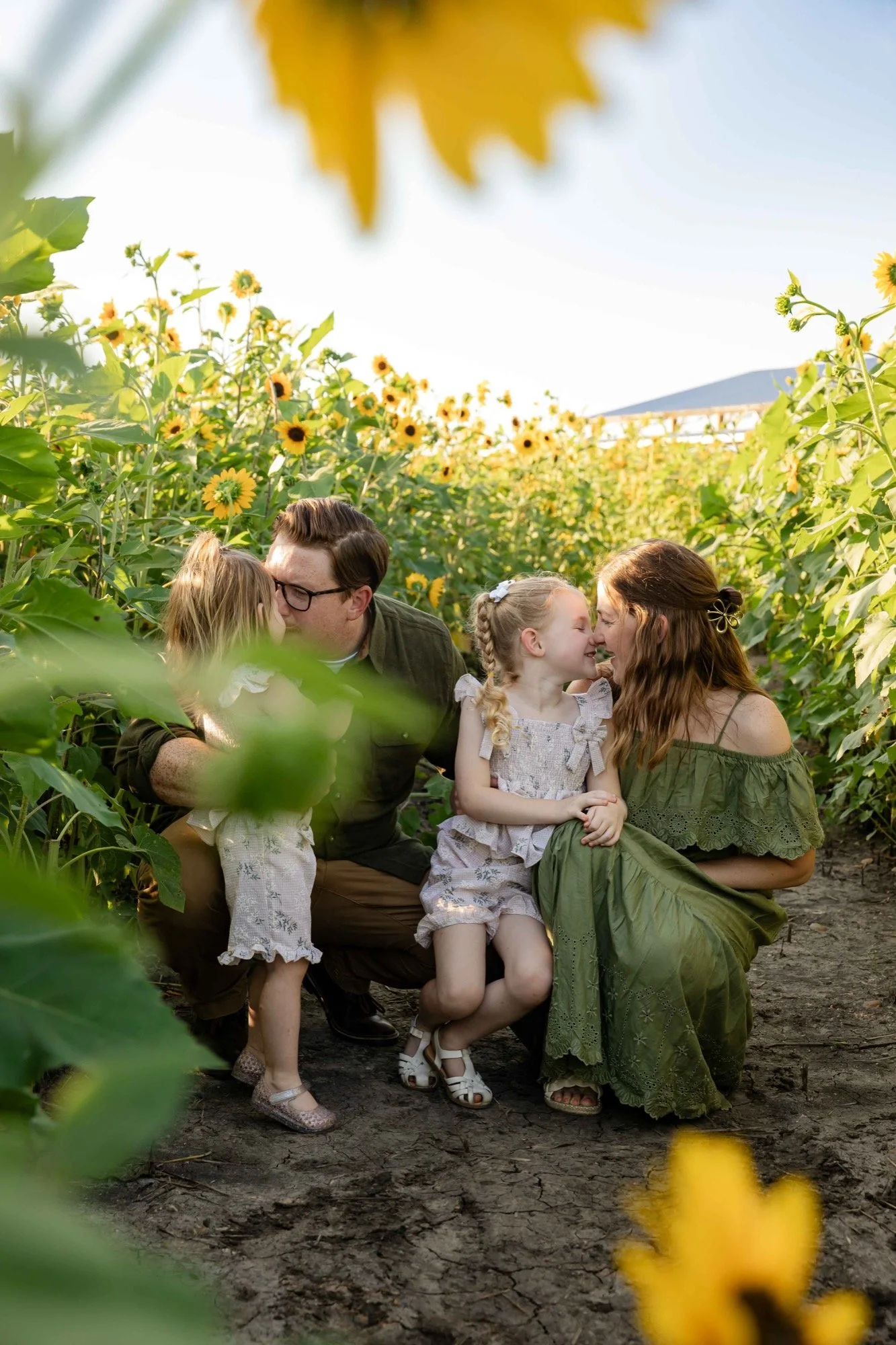 Family of four sharing a playful moment among sunflowers at Western Belle Farms in Central Texas.