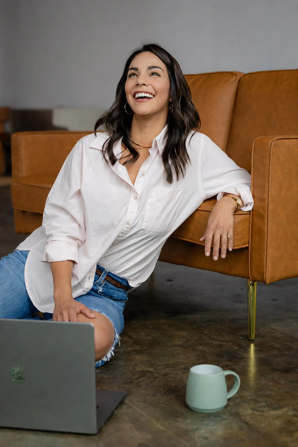 Woman in a white shirt sitting beside a tan leather chair with a laptop and coffee mug during a small business branding session at Sunroom Studio in downtown Waco, Texas.
