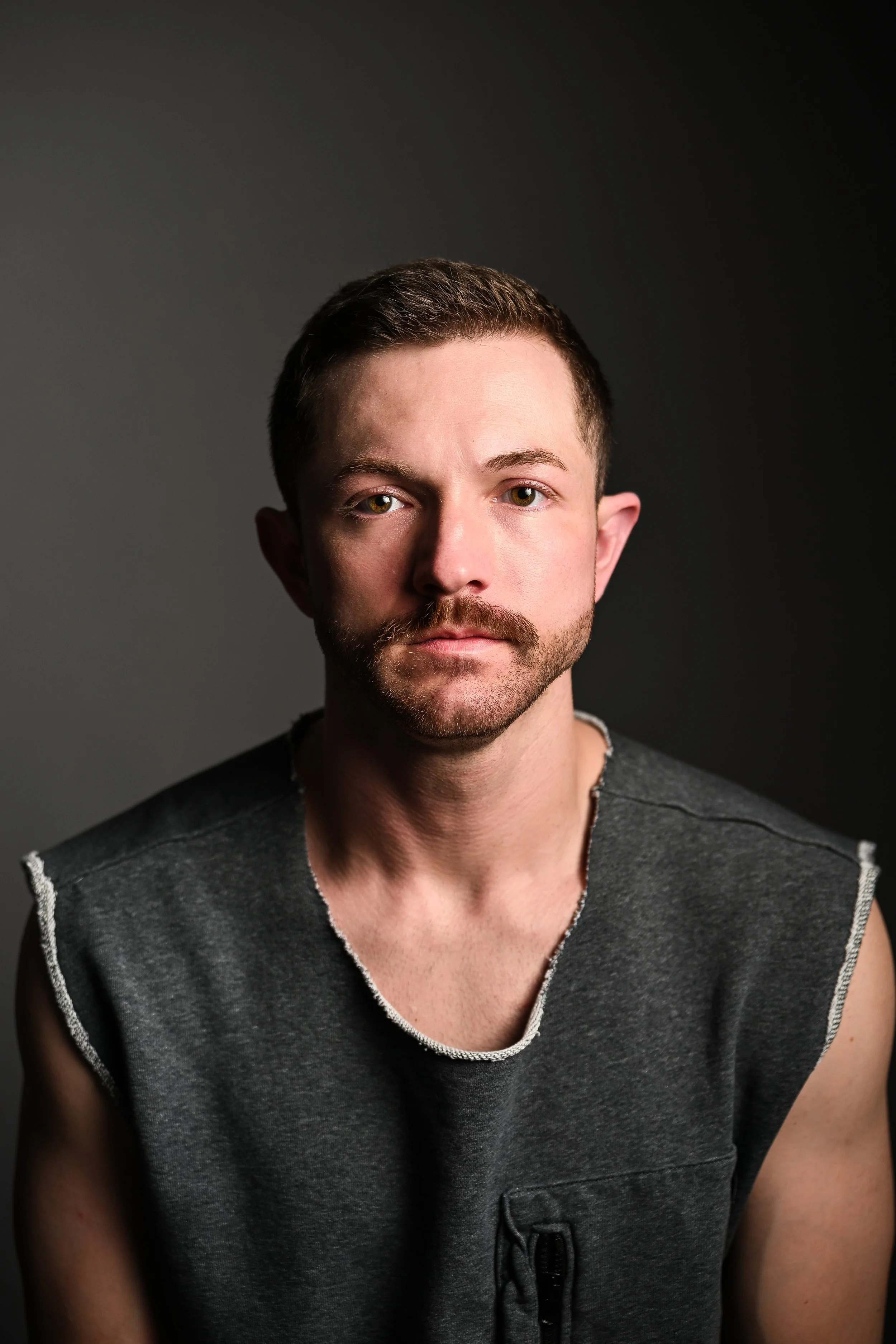 Editorial portrait of Jeremy in a charcoal sleeveless shirt against a dark studio background.