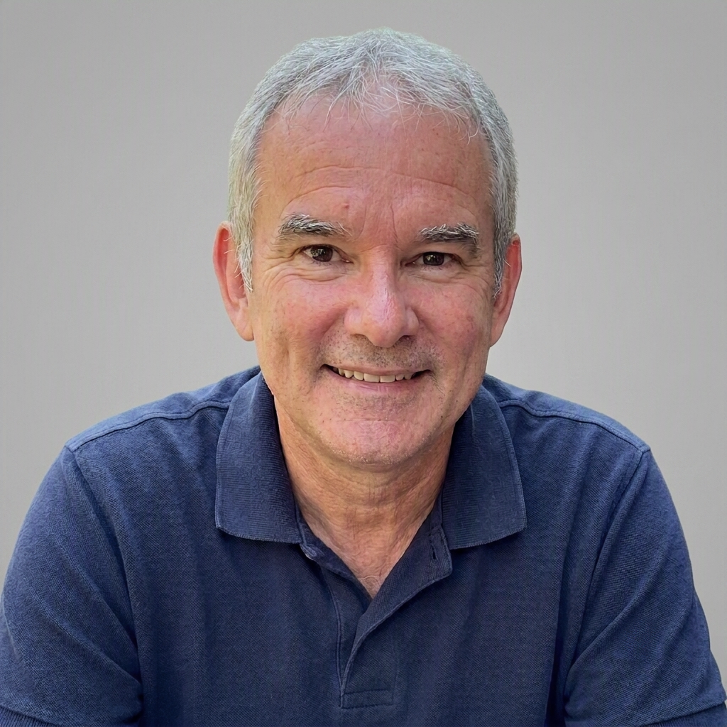 A smiling middle-aged man with gray hair and a blue collared shirt, sitting against a plain background.