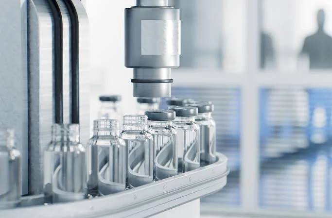 Automated laboratory equipment filling small glass bottles with liquid.