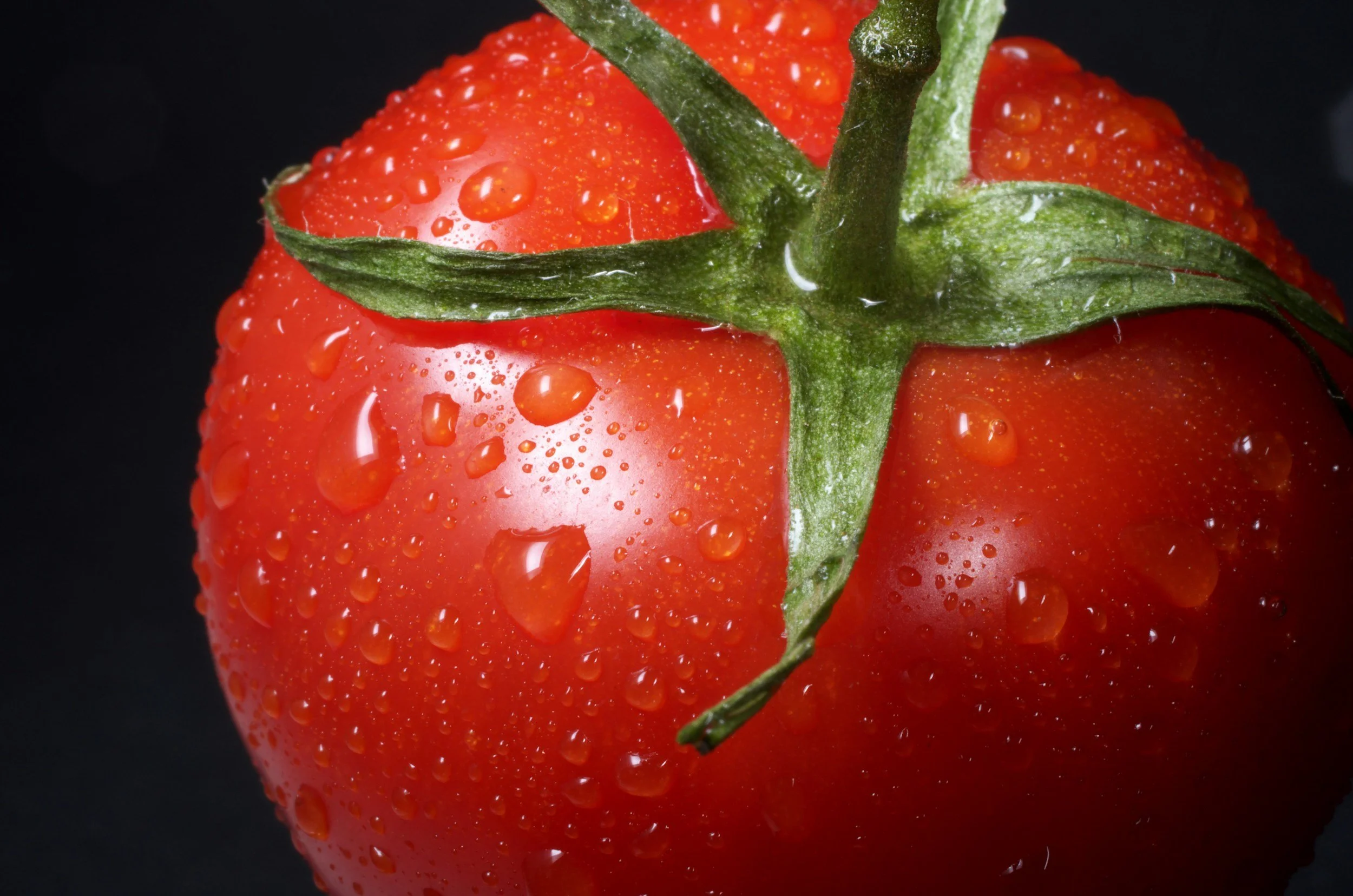 Close-up of a ripe red strawberry with water droplets on its surface, against a black background.