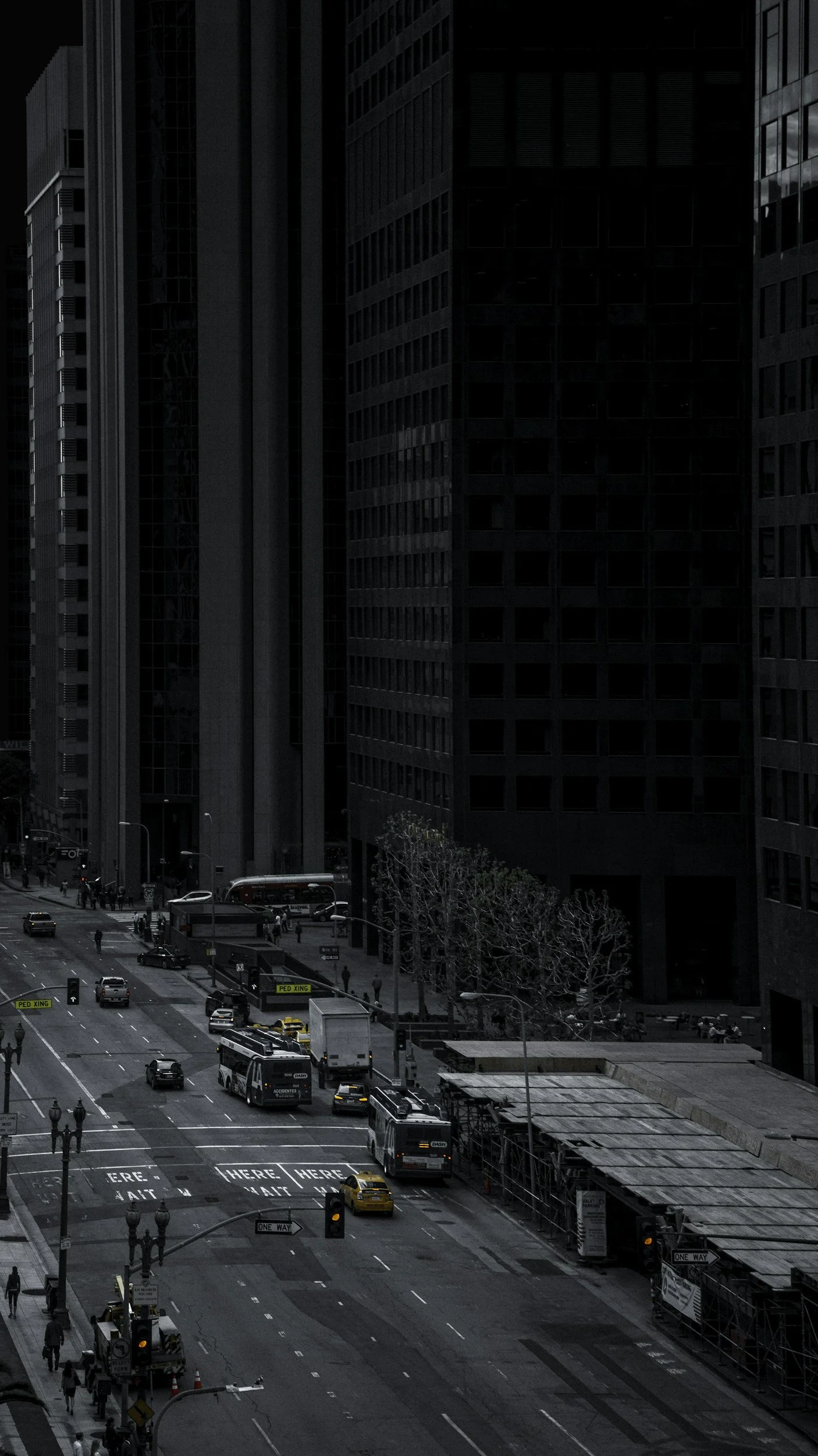 City street scene with tall dark buildings, cars, buses, people walking, traffic lights, and crosswalks in an urban area.