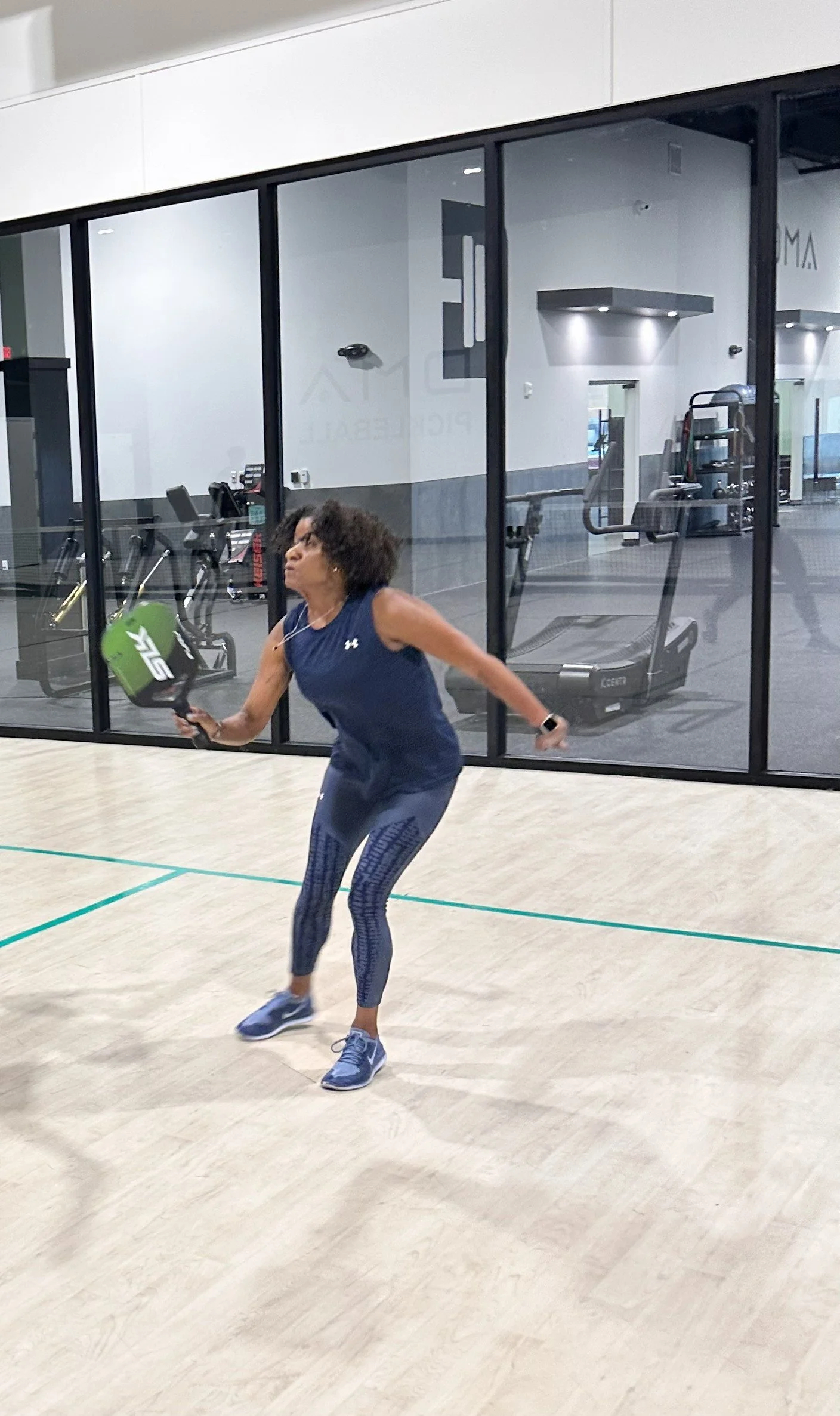 Bernadette Douglas, wellness coach and founder of Soulful Health Coach  playing pickleball in a gym, with exercise equipment and gym walls visible in the background.