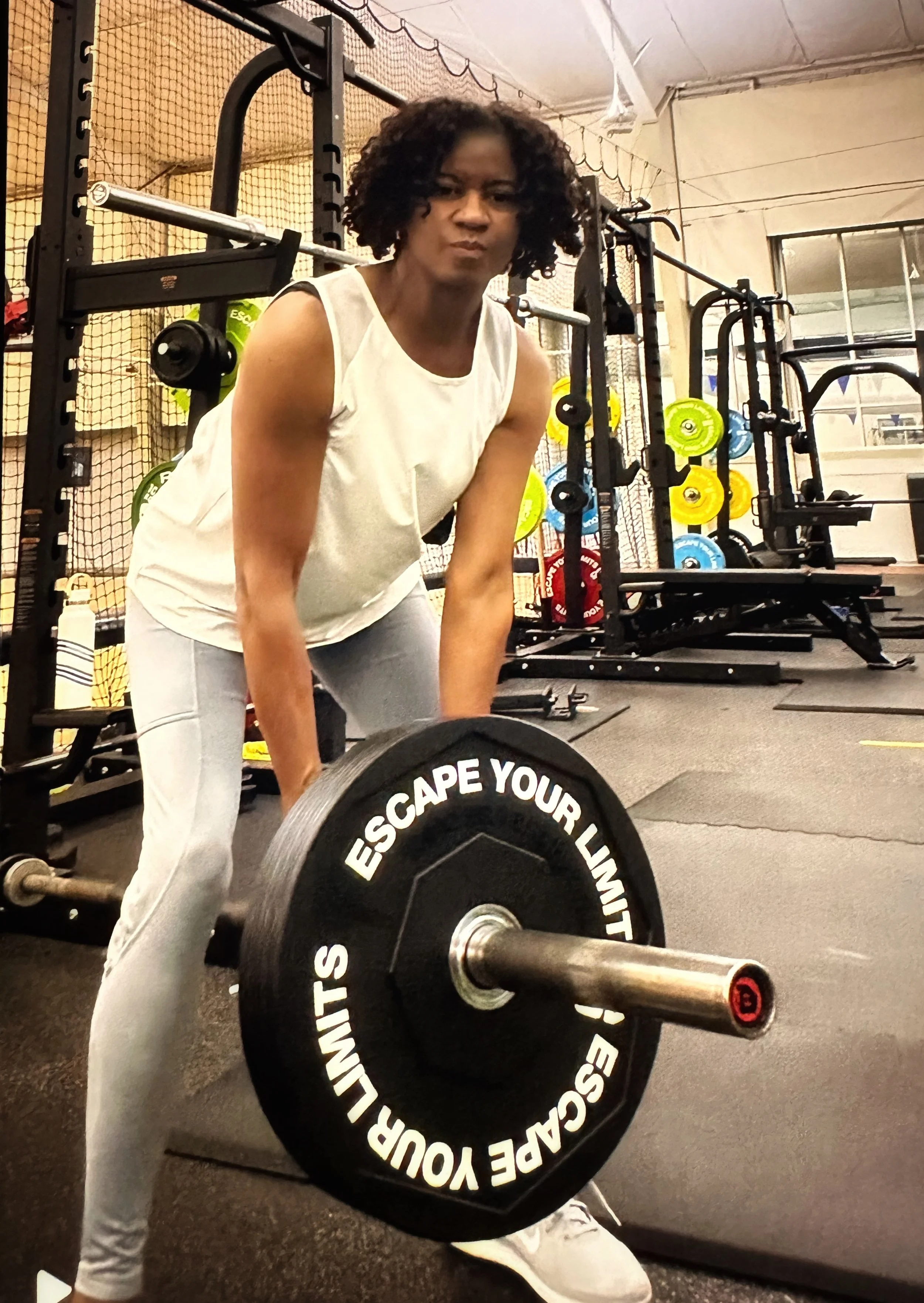 Bernadette Douglas, wellness coach and founder of Soulful Health Coach lifting a barbell at the gym surrounded by gym equipment and colorful weight plates.