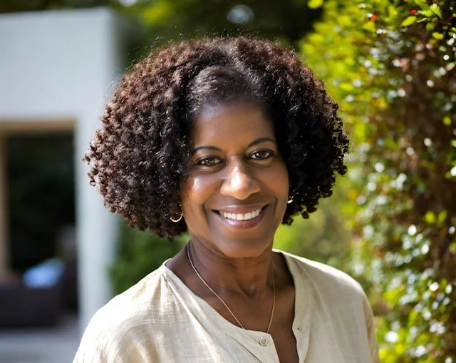 Bernadette Douglas, wellness coach and founder of Soulful Health Coach standing outdoors in front of green foliage.