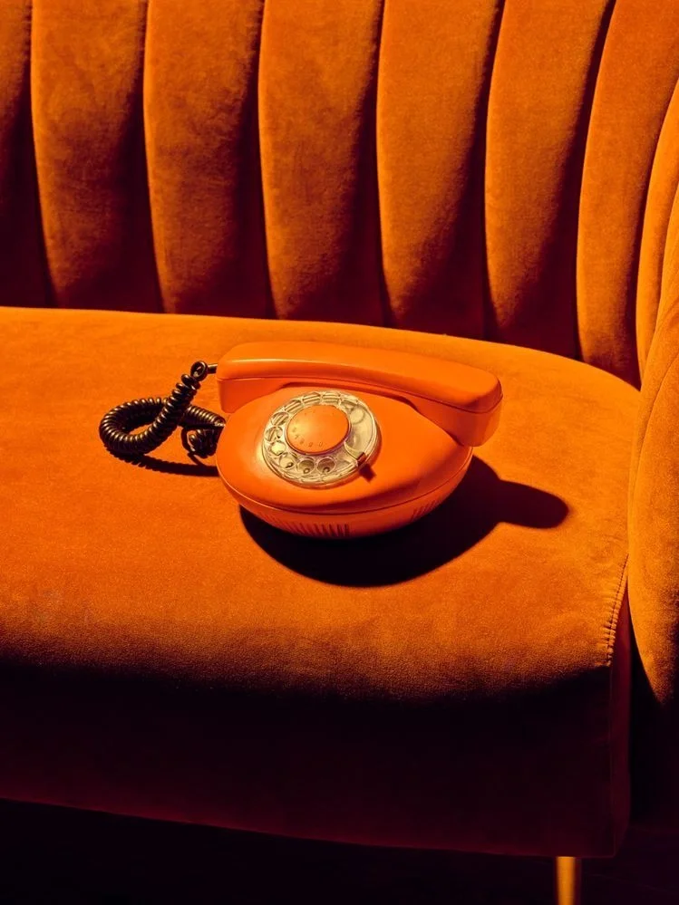 An orange rotary phone resting on a vintage orange velvet sofa.