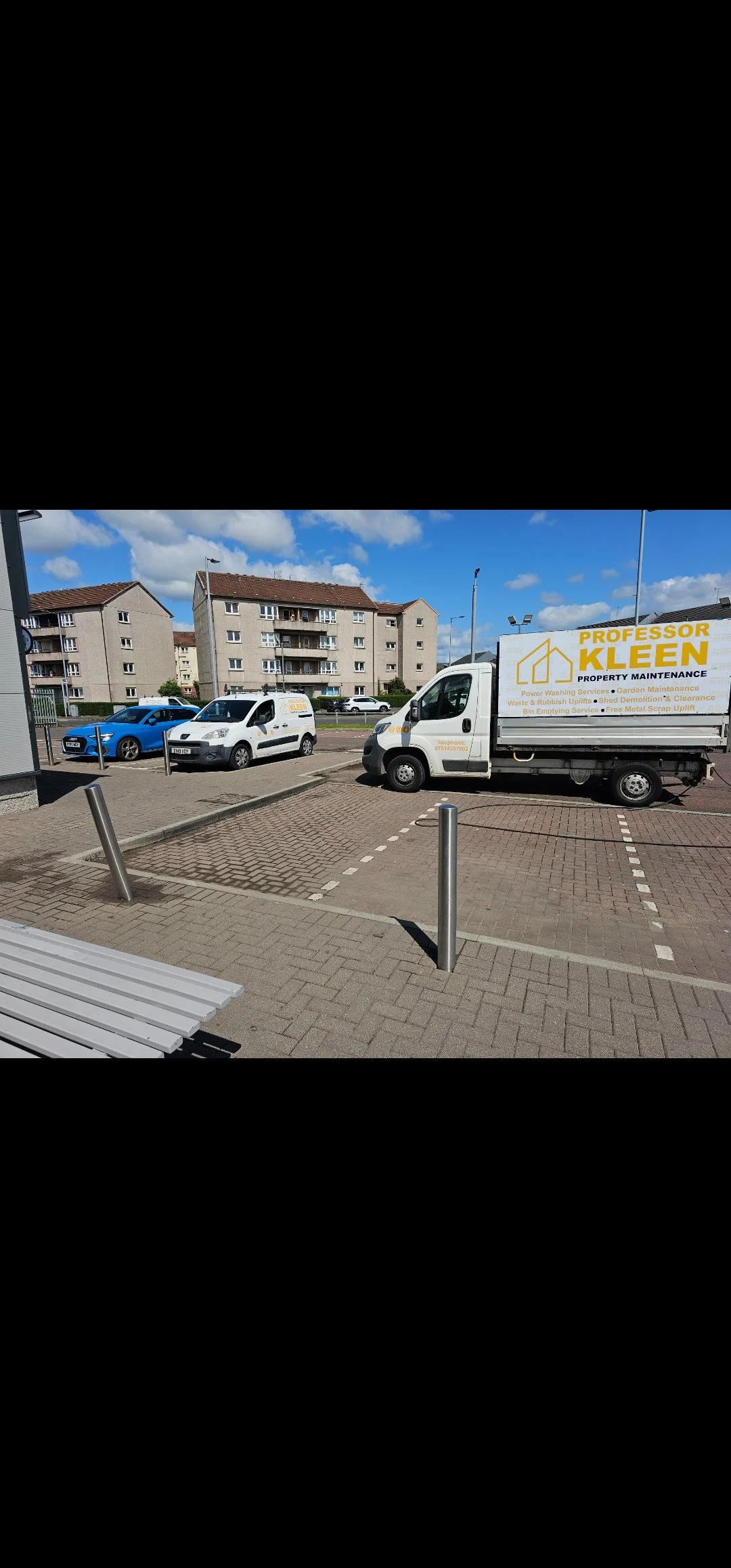 Parking lot with parked vehicles, including a white van with a company logo for property maintenance, and residential buildings in the background under a partly cloudy sky.