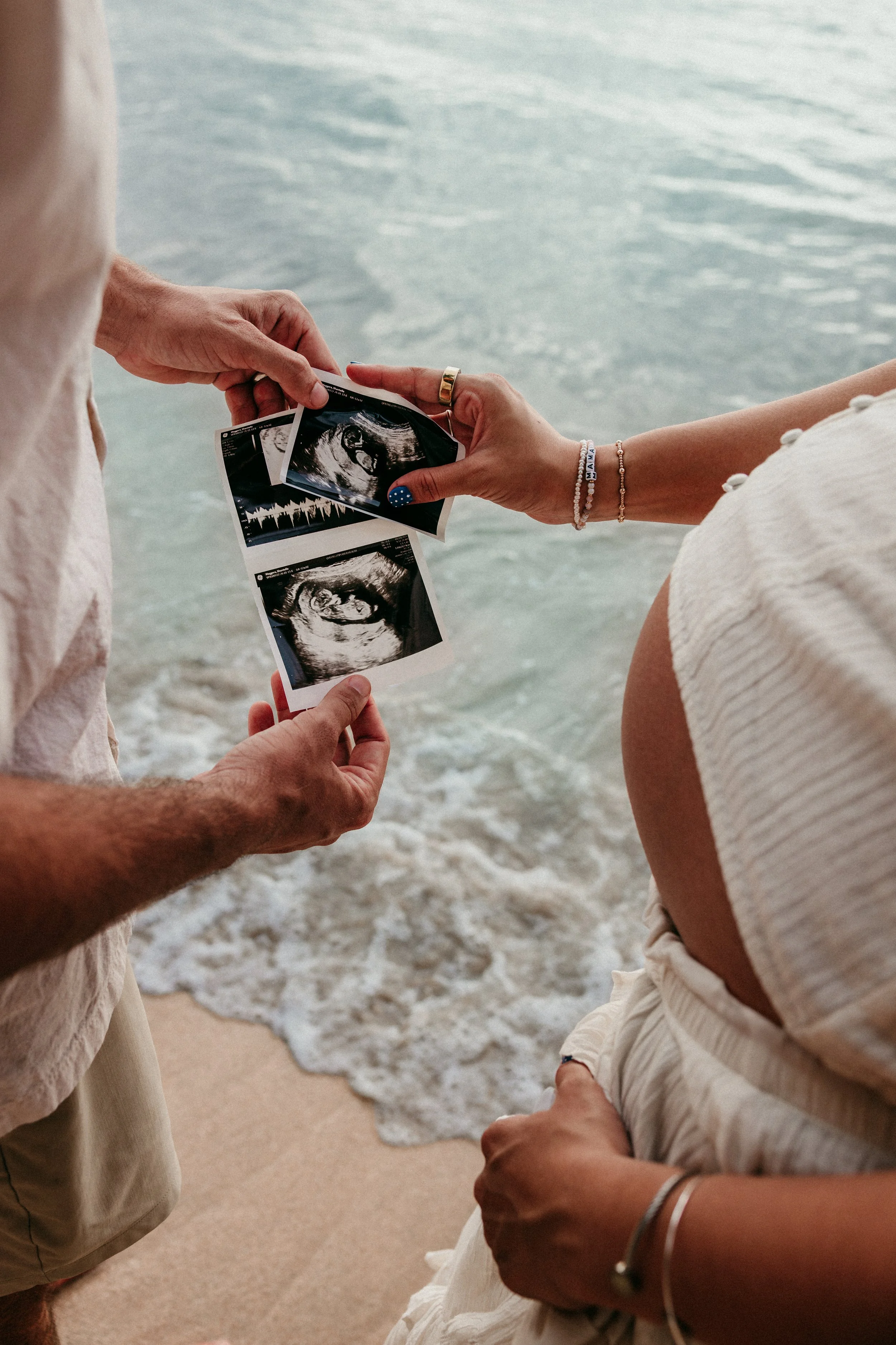 Person holding ultrasound images of a developing fetus at the beach near the water.