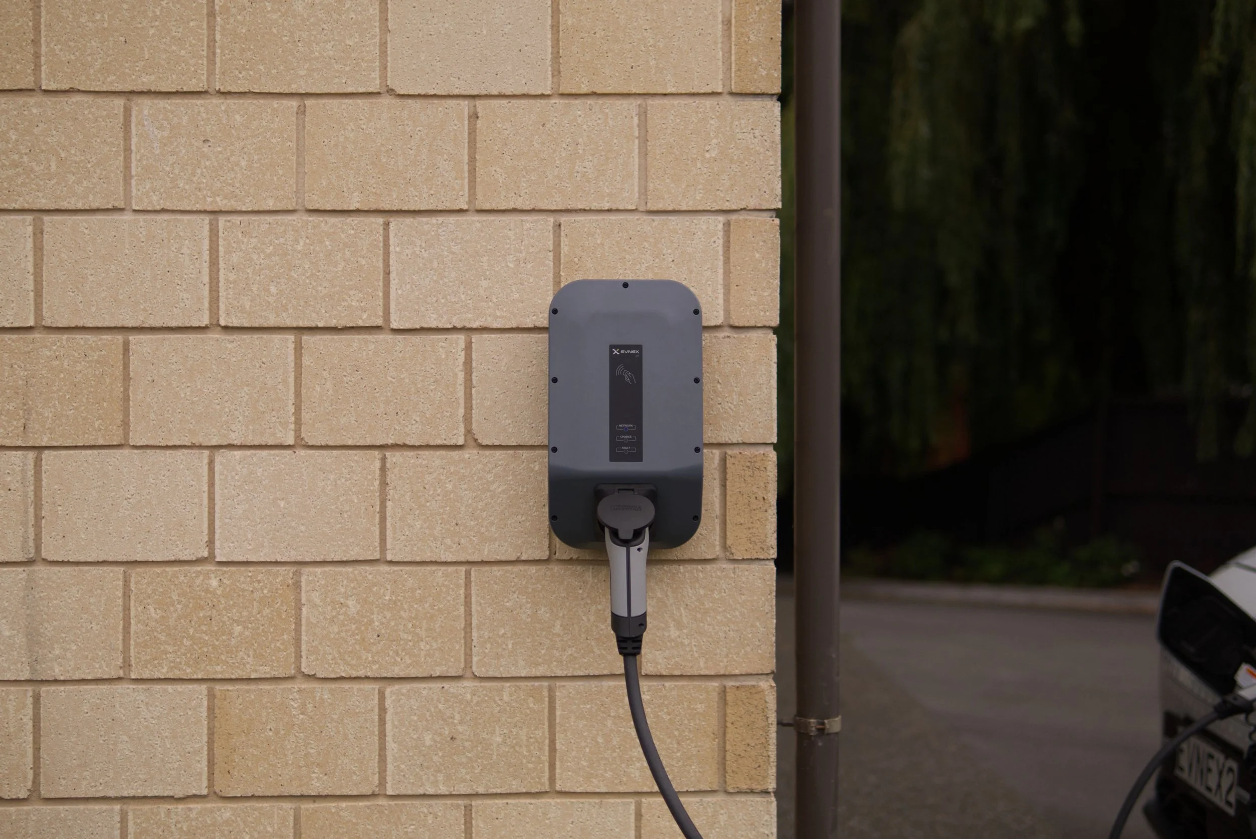 Electric vehicle charging station mounted on a beige brick wall outdoors.