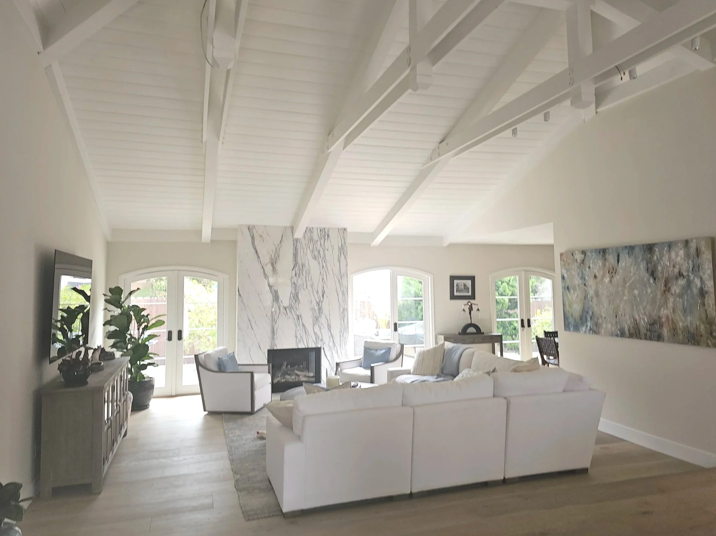 Living room with white sectional sofa, marble fireplace, light wood flooring, large windows, and various art pieces.