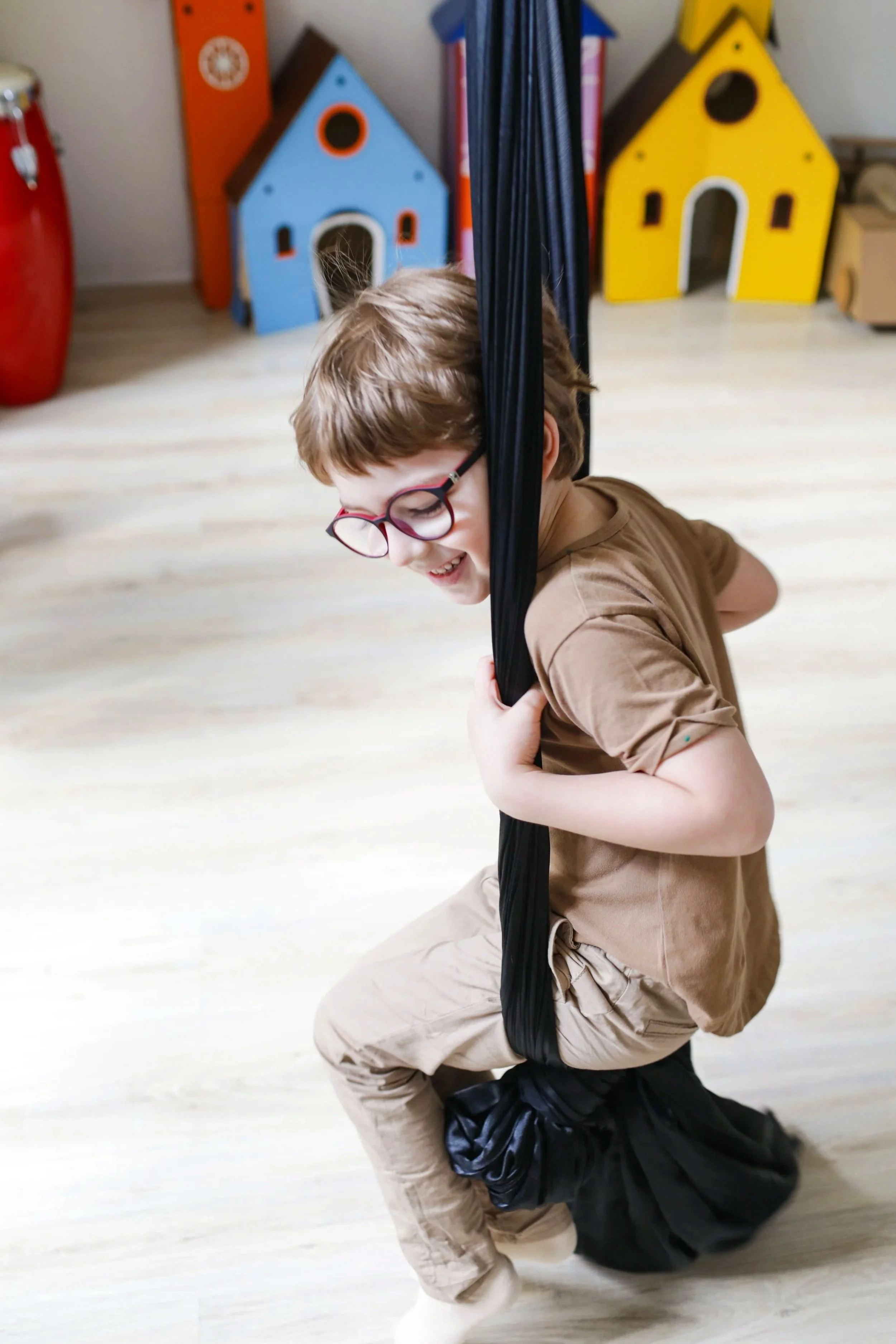 An autistic boy with glasses smiling while on a sensory swing at AltPlay, an inclusive, sensory play-gym in Orange County, CA