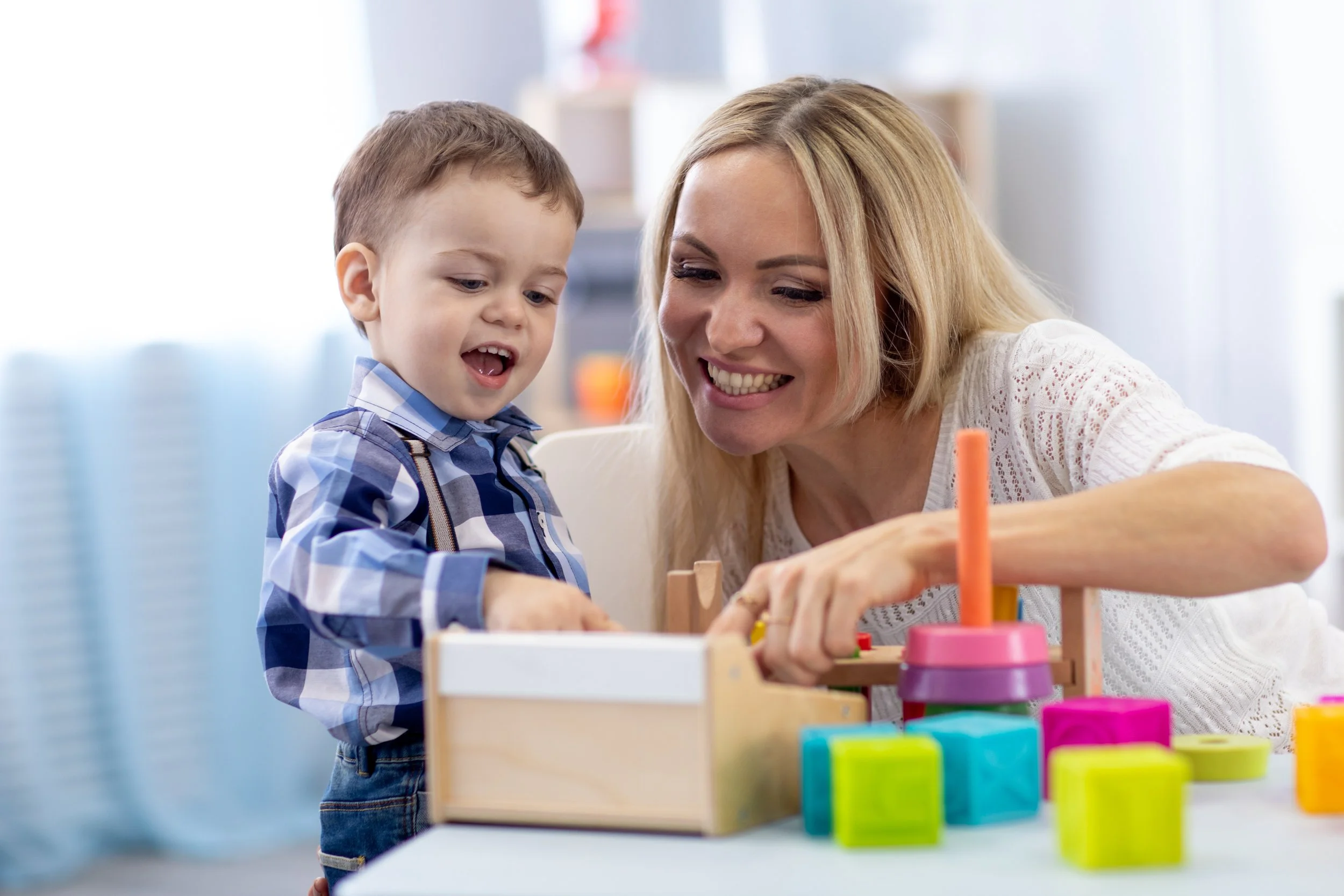 An occupational therapist and a young boy playing with colorful toy blocks at a table. The occupational therapist is using the sensory-friendly space at AltPlay, an inclusive play gym in Orange County, CA