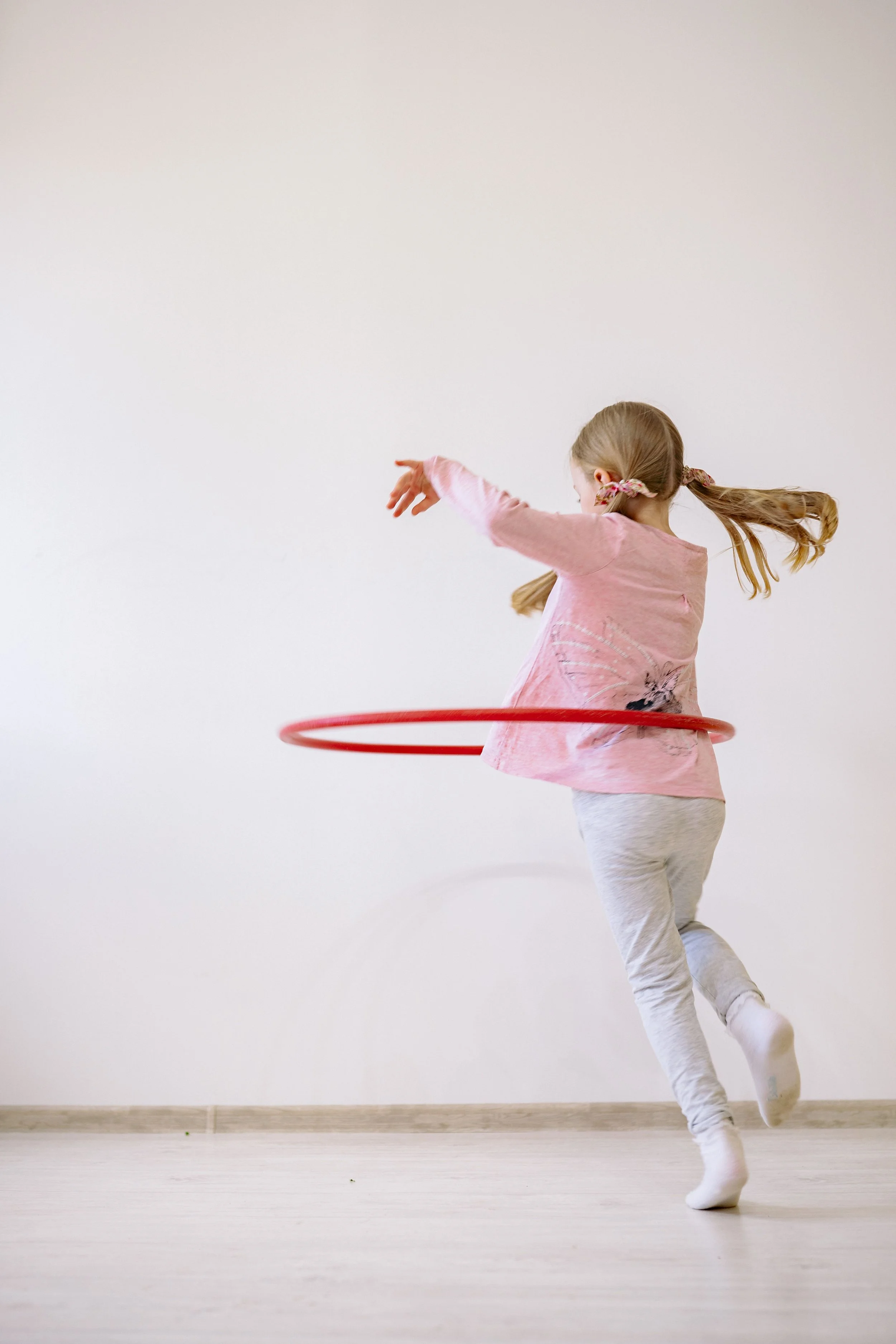 A young girl with blonde hair, spinning inside a pink hula hoop, during sensory play at AltPlay indoor play gym in Orange County, CA