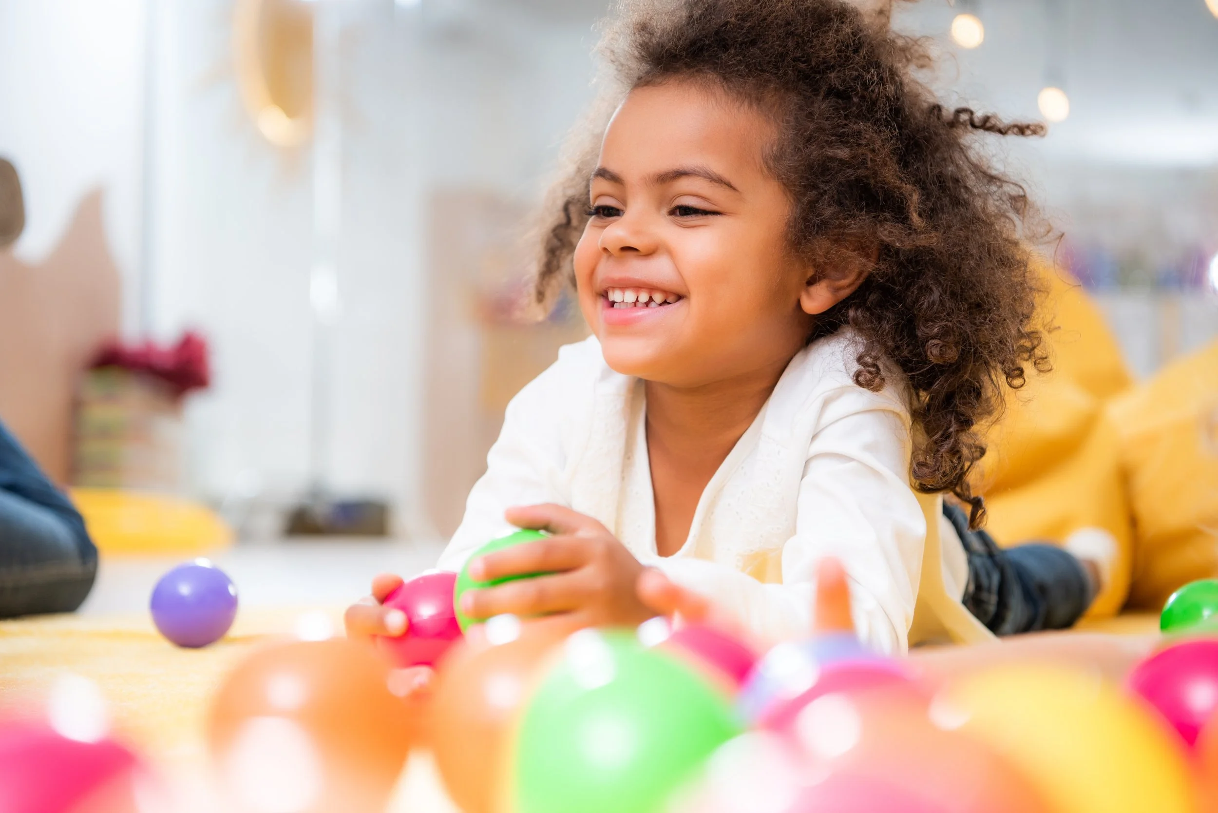 A young girl with curly hair smiling working on sensory integration while playing with colorful toys at a sensory play gym in Orange County, CA