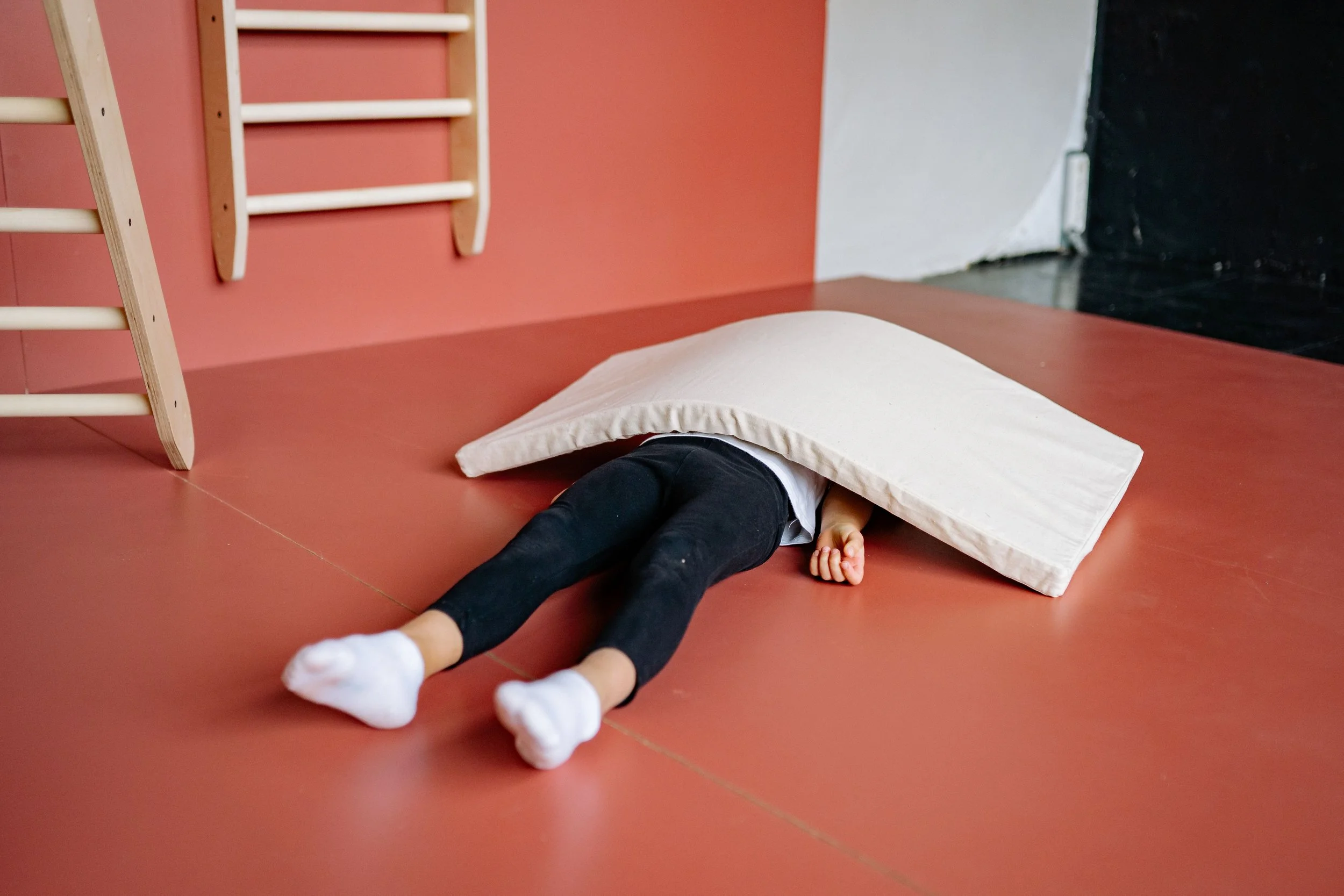 Child working on sensory regulation at an indoor, sensory play gym in Orange County, CA, lying in a room with wooden ladders and other sensory play items.