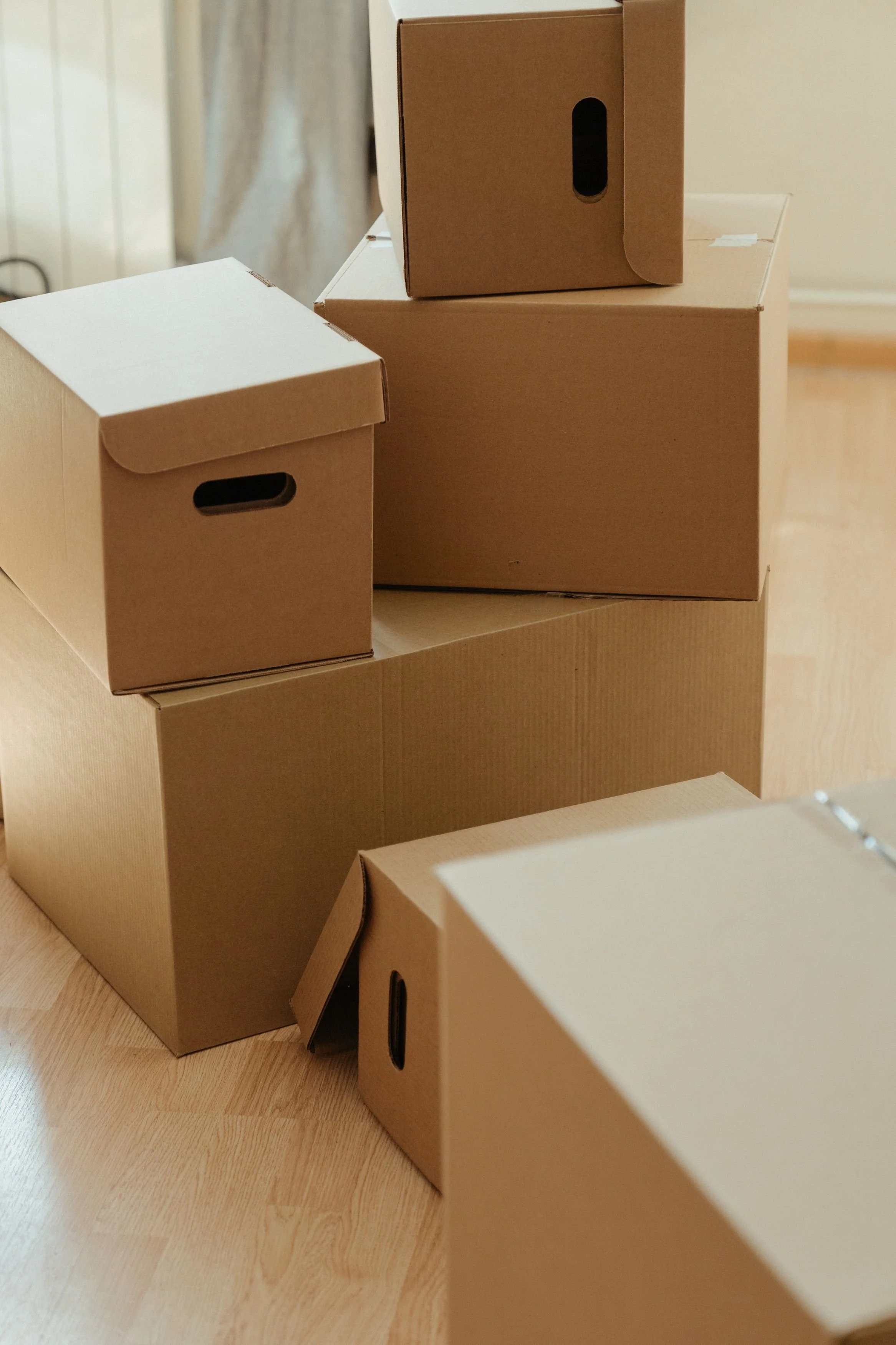 Several cardboard boxes, some with cutouts, stacked on hardwood floor in a room with light-colored walls.