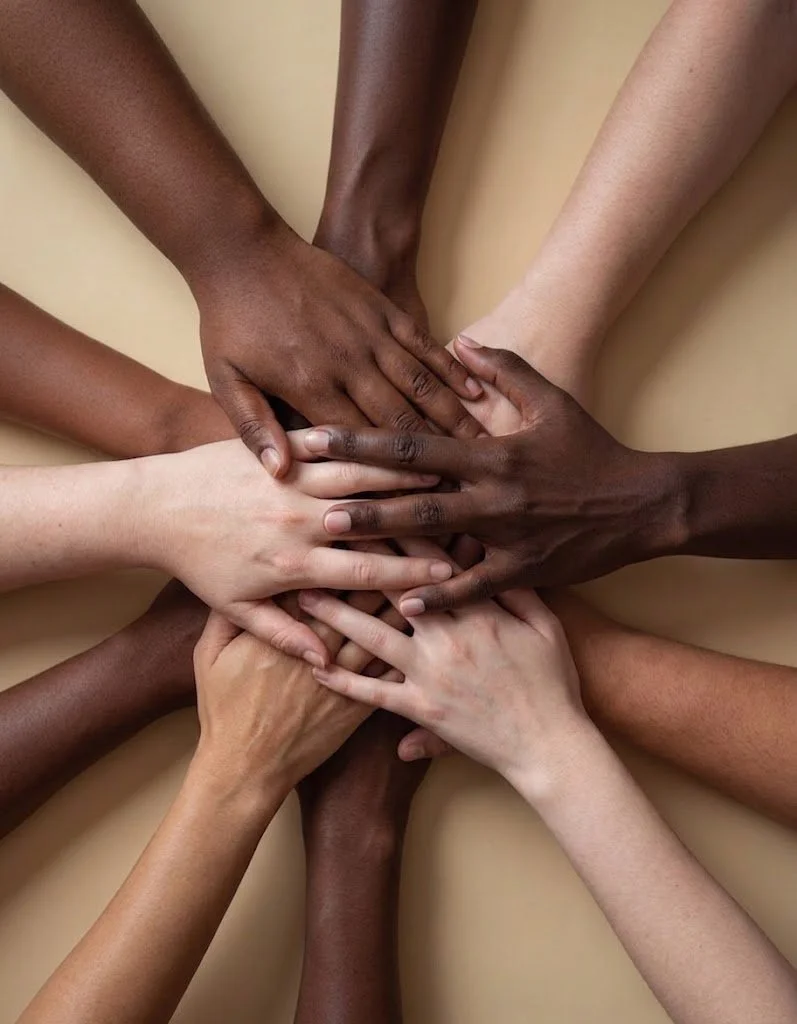 Multiple hands of different skin tones stacked together in a circle, palm to palm.