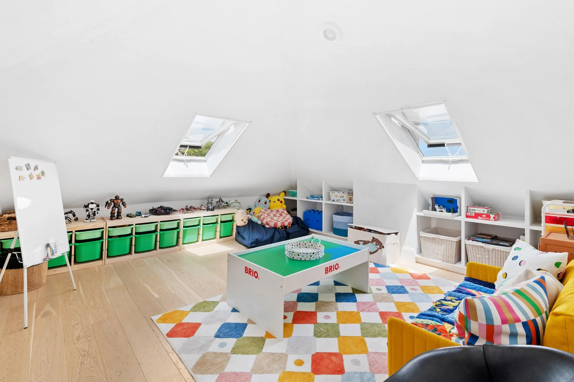 Brightplayroom with colorful carpet, toys, and stuffed animals, featuring skylights and white shelving units.