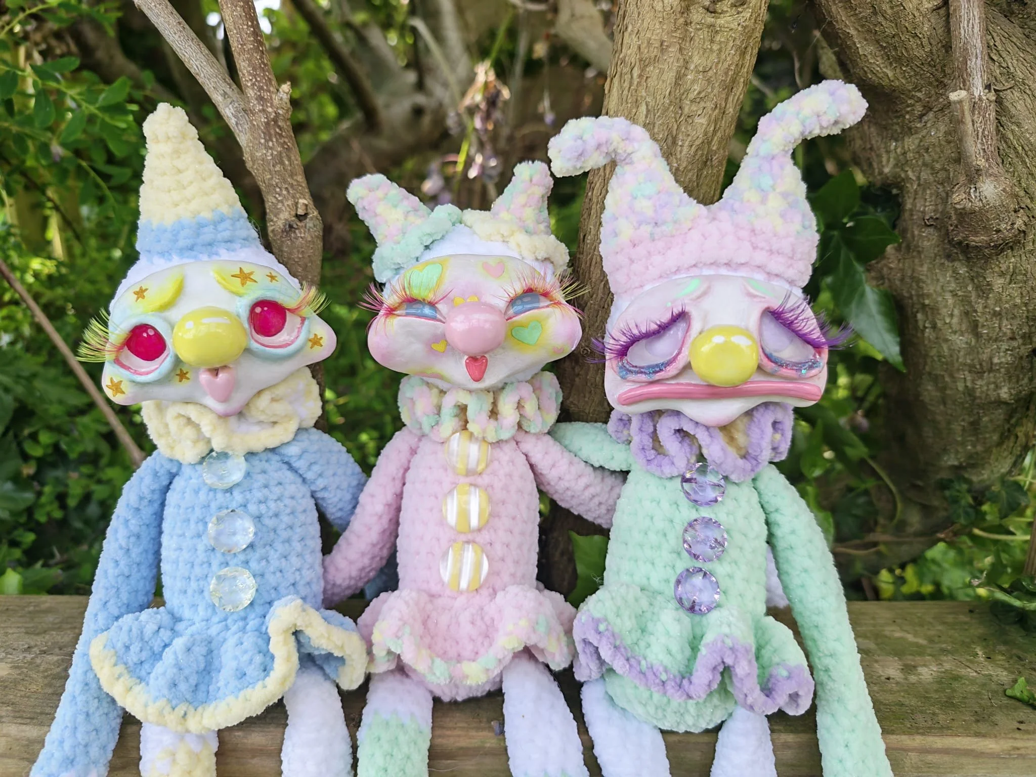 Colorful plush toy bunnies with quirky facial features and long ears hanging on a tree branch.