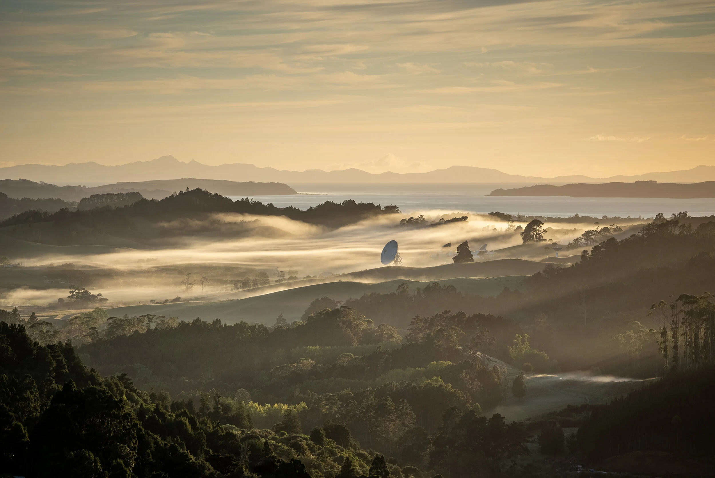 Golden sunrise over misty rolling hills with trees and distant valleys.