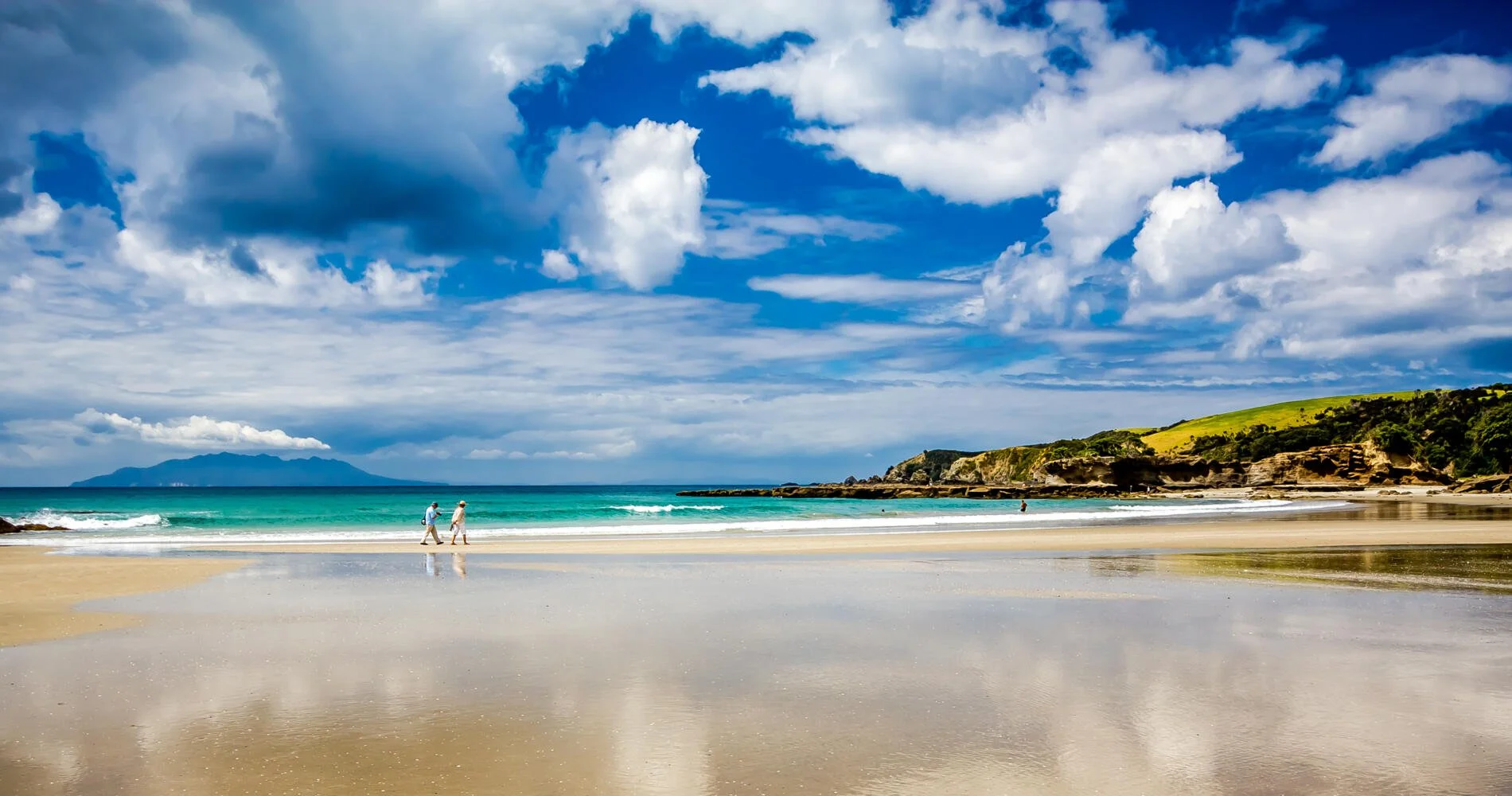 Golden sand beach with turquoise water and dramatic clouds.