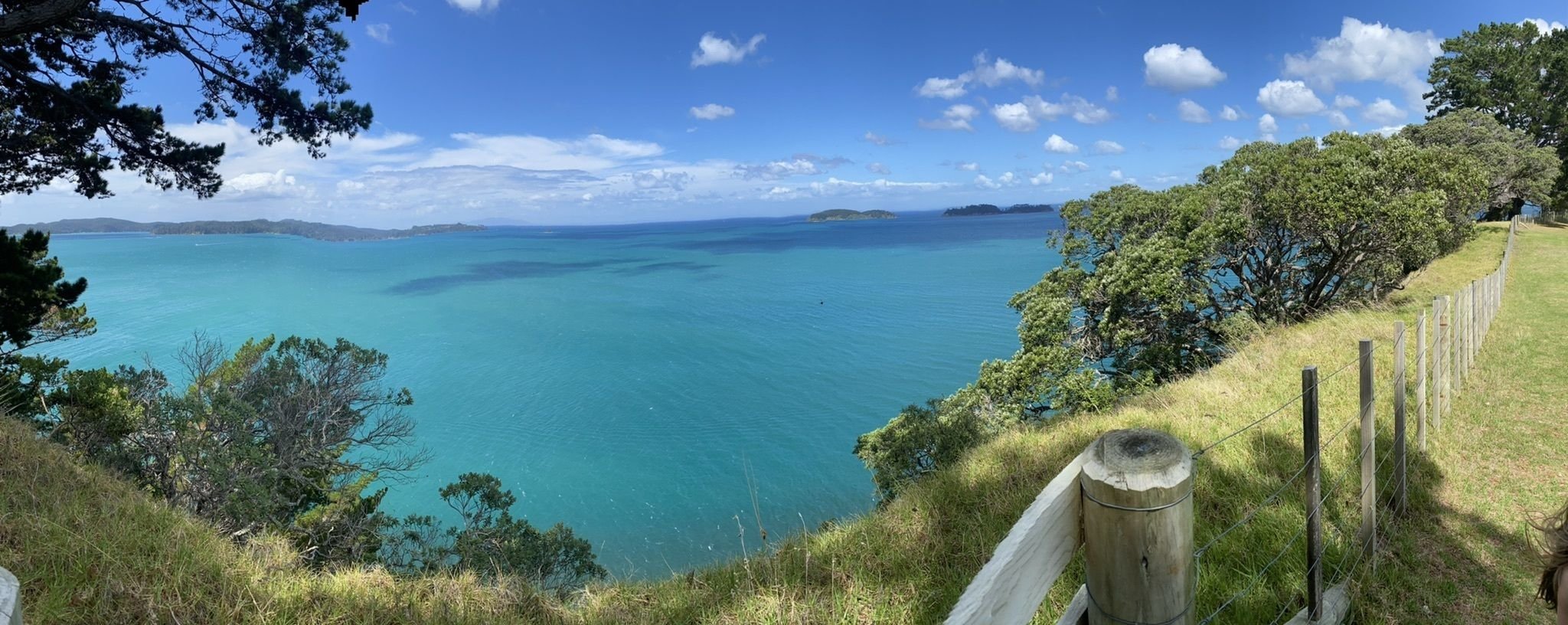 Panoramic coastal view overlooking turquoise ocean waters, rolling hills, and offshore islands under a blue sky.