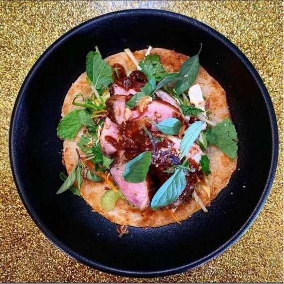 Plated gourmet dish with sliced meat, fresh herbs and rich sauce.