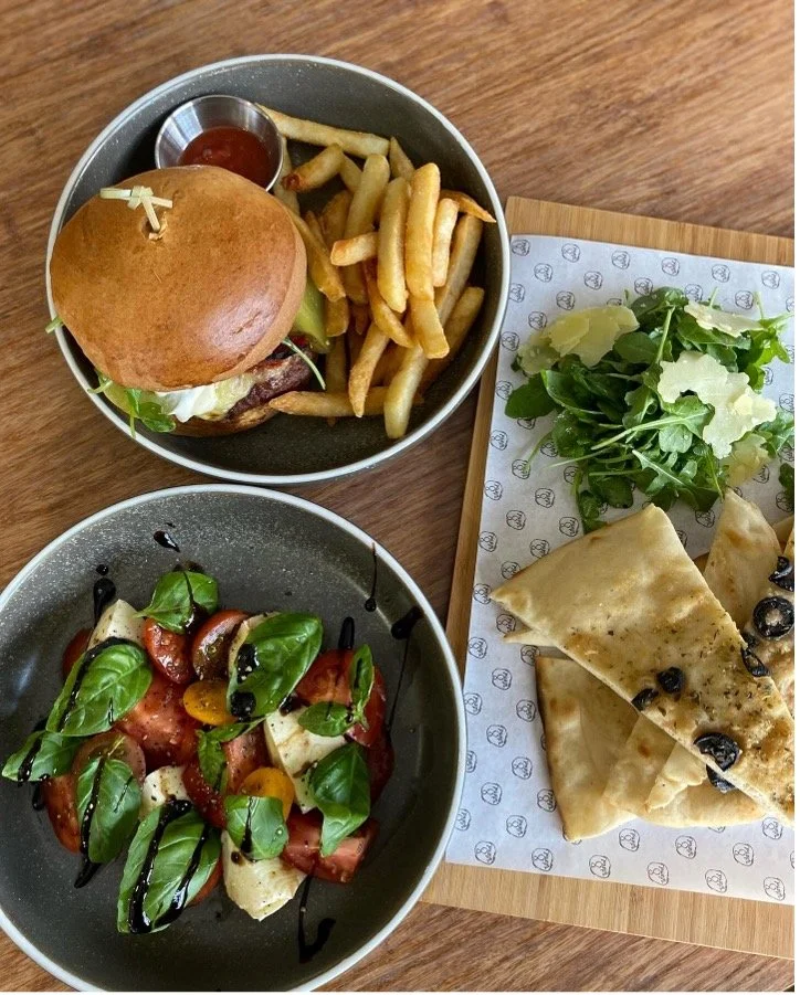 Burger with fries, fresh salad and shared plates on a wooden table.