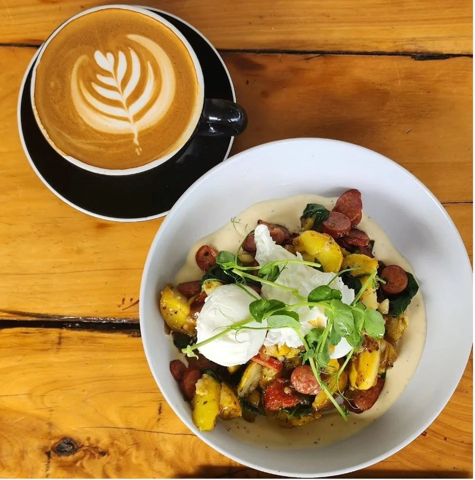 Latte coffee with brunch bowl topped with sausage, potatoes and poached eggs.