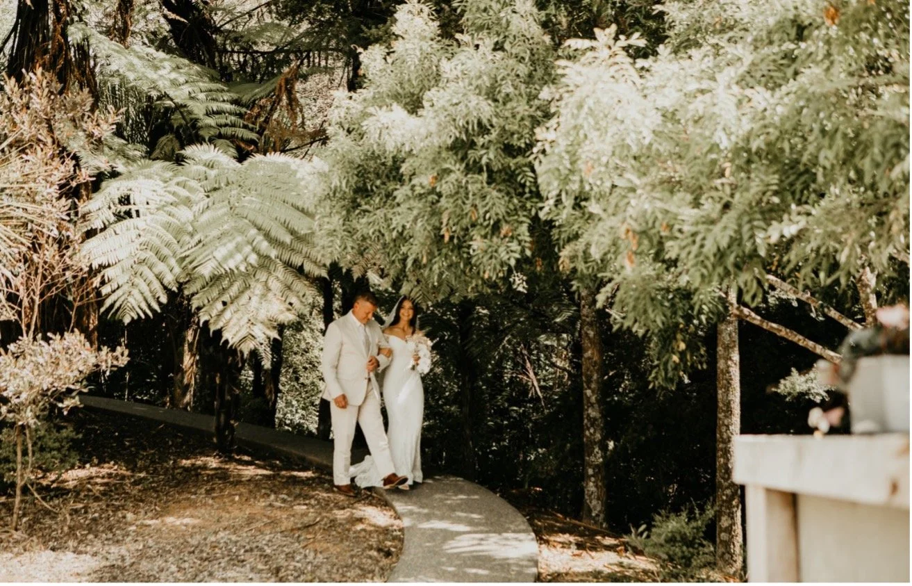 Couple walking through forest gardens at a luxury wedding venue on the Matakana Coast near Warkworth, New Zealand.
