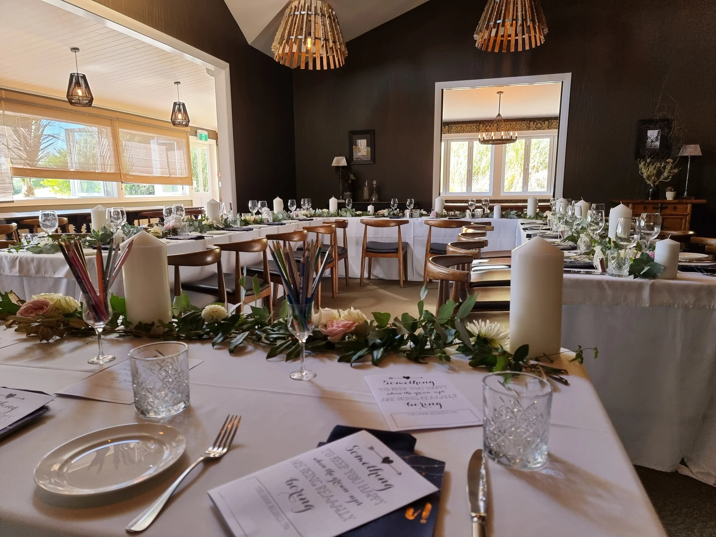 Wedding reception room styled with long banquet tables, candles, greenery and elegant table settings.