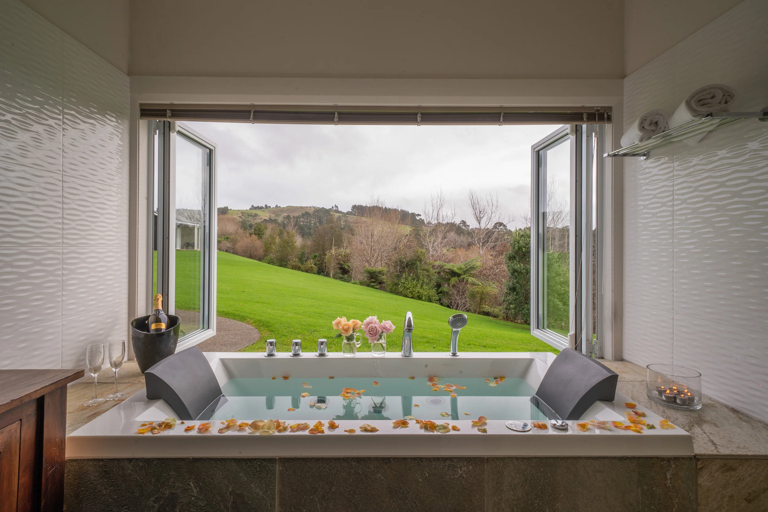 Freestanding bathtub beside open windows offering lush garden views and natural light.