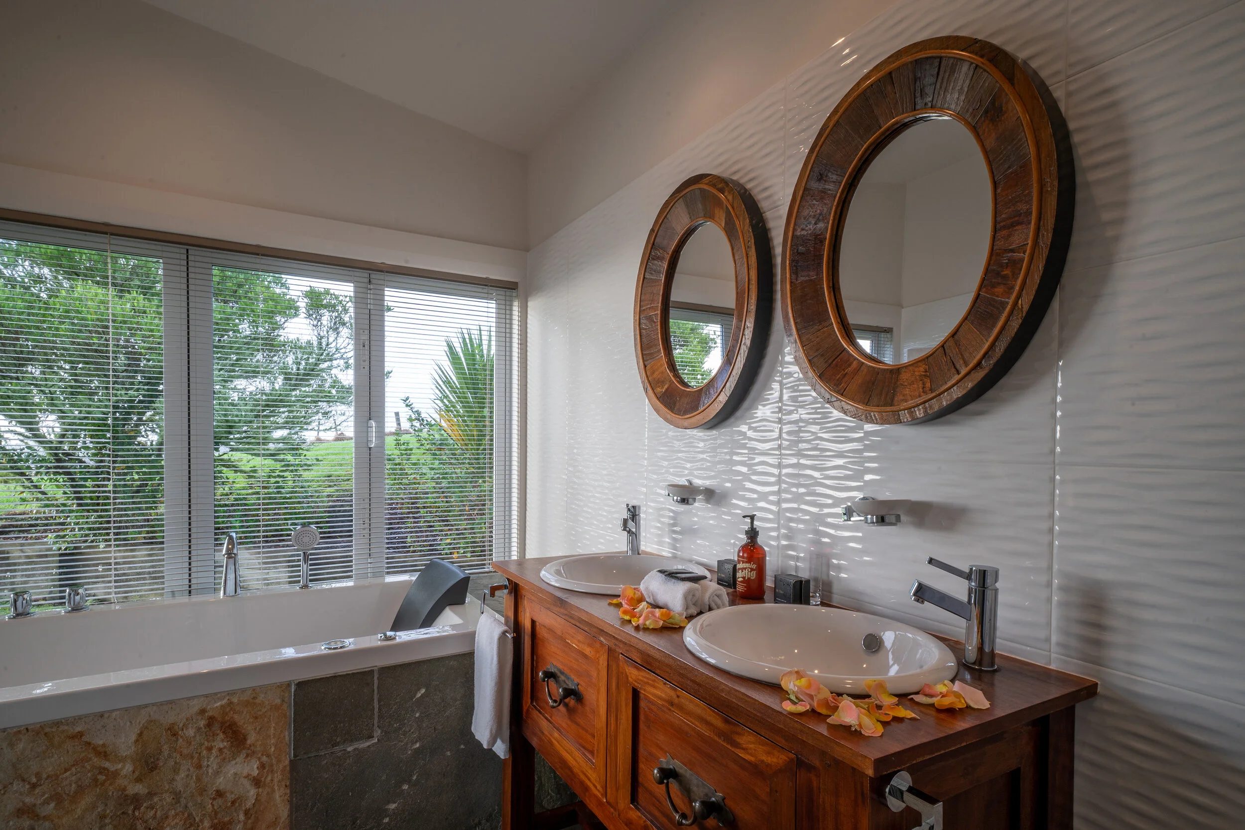 Luxury bathroom with twin mirrors, double sinks, and wooden vanity under bright daylight.