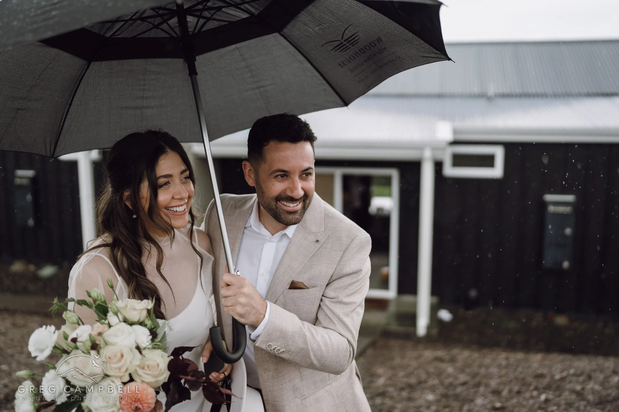 Smiling couple under an umbrella, celebrating love despite the rain in a beautifully intimate moment.