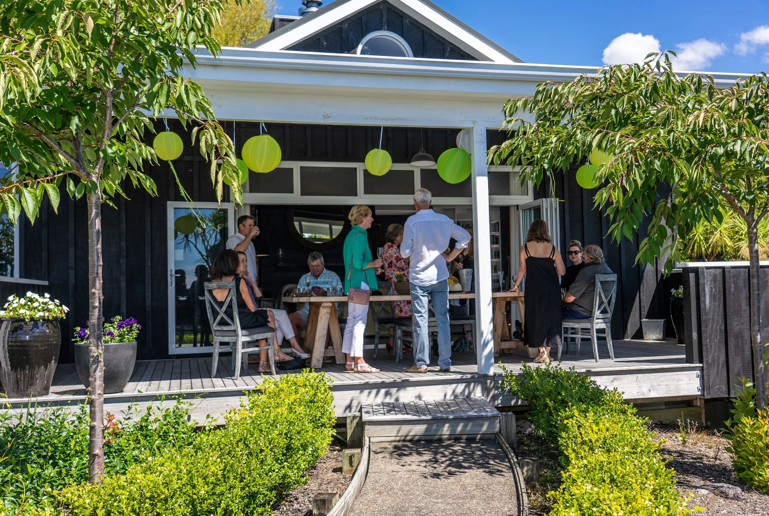 Guests gathering on the outdoor veranda at Woodhouse Mountain Lodge in Matakana surrounded by landscaped gardens.