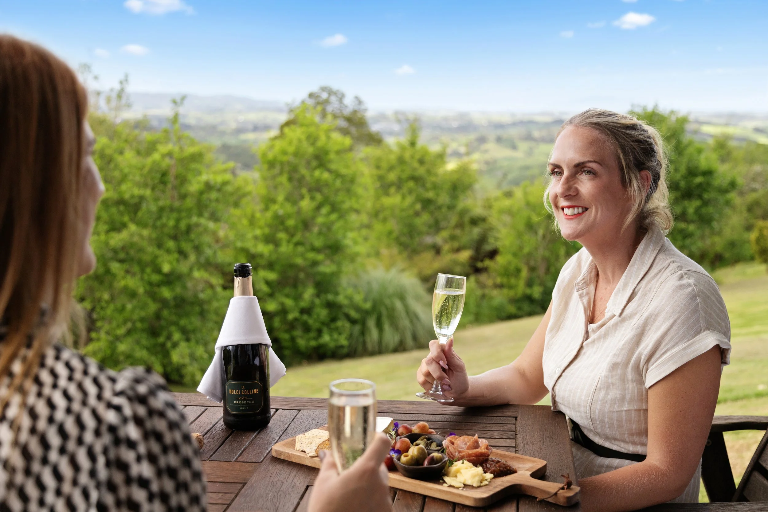 Guests enjoying wine and a grazing platter overlooking the Matakana countryside at Woodhouse Mountain Lodge.