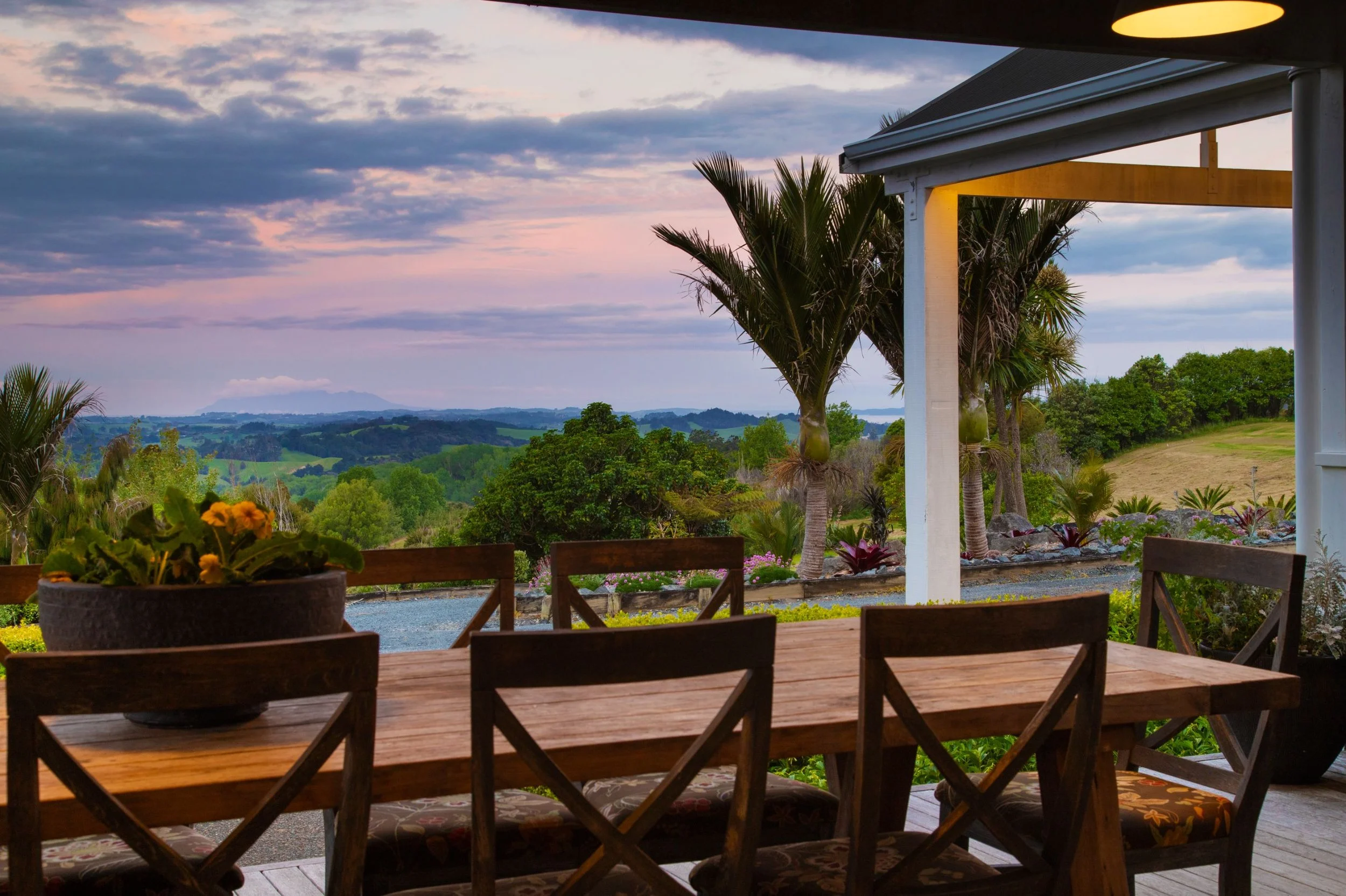 Outdoor dining terrace at Woodhouse Mountain Lodge overlooking the Matakana countryside at sunset.