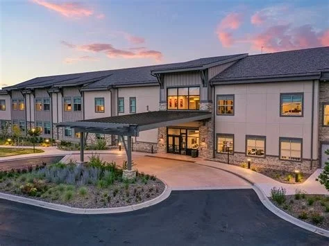 Exterior view of a modern apartment building during sunset with a curved driveway and landscaped garden in front.