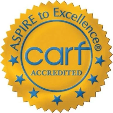 Gold and blue CARF accreditation badge with the words 'Aspire to Excellence' and 'Accredited'.